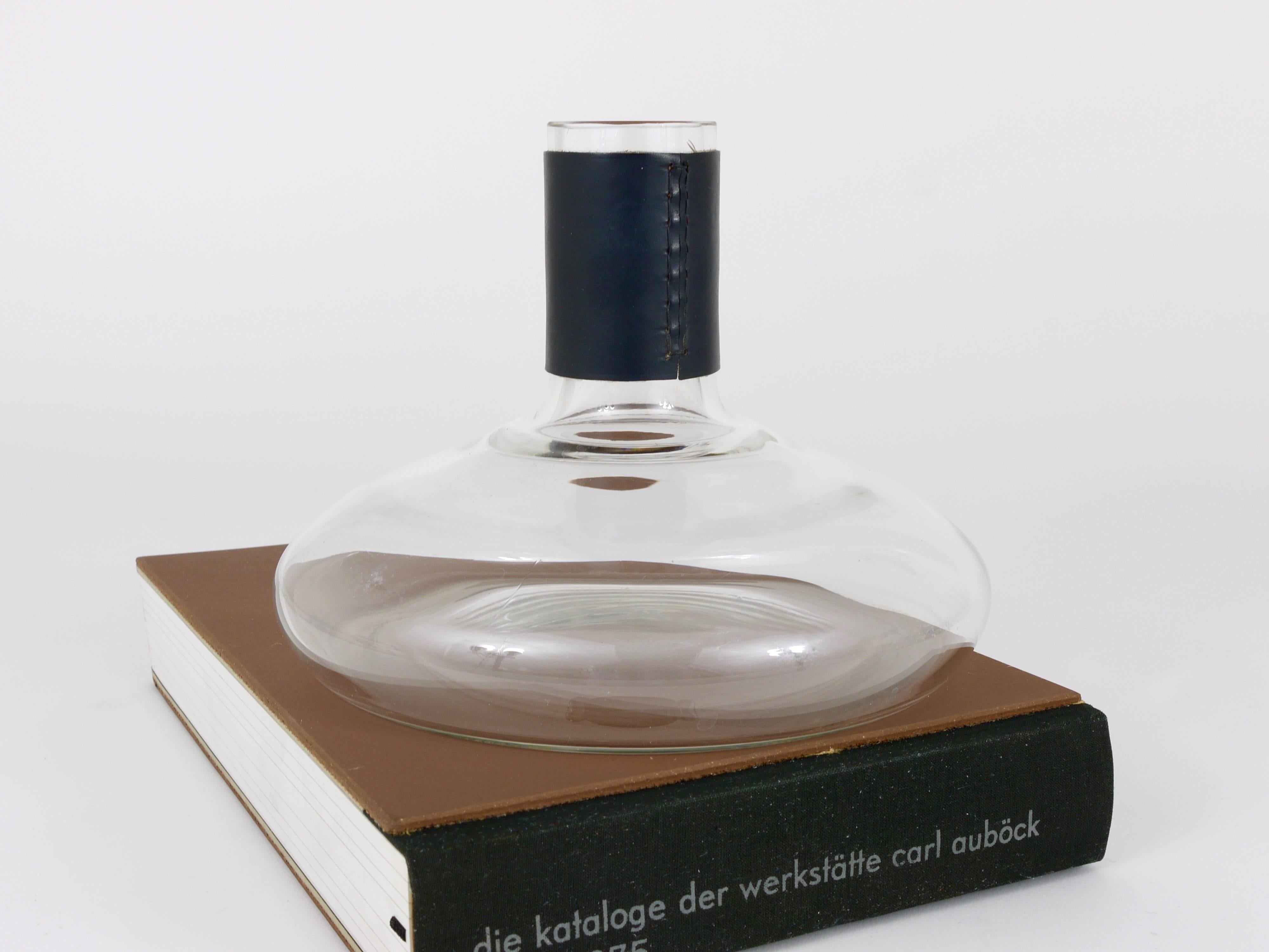 A beautiful Austrian modernist flower vase or wine decanter designed and executed by Carl Auböck in the 1950s. Made of glass with nice black leather top. In very good condition. Measure: Height 6 1/2 in, diameter 8 1/2 in.