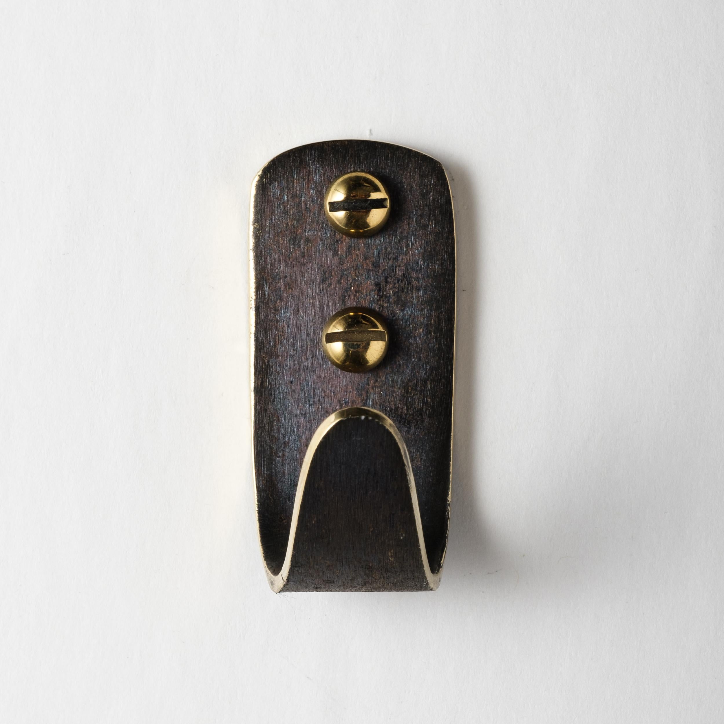 Carl Auböck model #4330/1 patinated brass hook. Designed in the 1950s, this versatile and Minimalist Viennese hook is executed in patinated and polished brass by Werkstätte Carl Auböck, Austria. 

Produced by Carl Auböck IV in the original Auböck