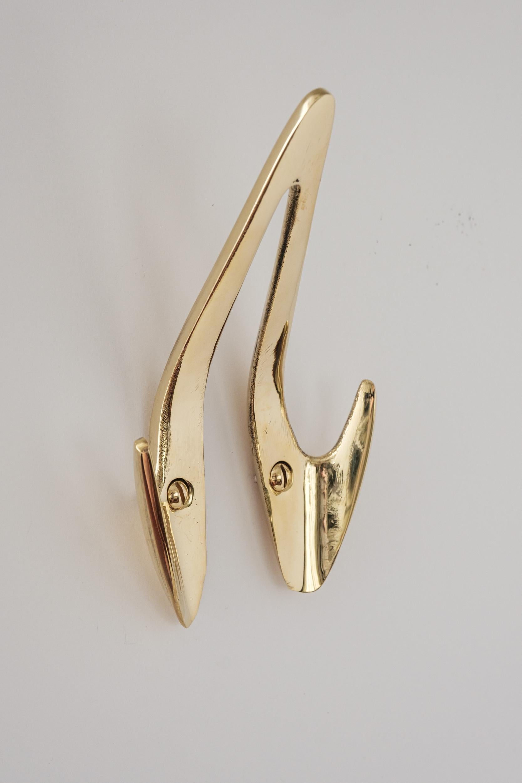 Carl Auböck Model #4994 polished brass hook. Designed in the 1950s, this versatile and Minimalist Viennese hook is executed in polished brass by Werkstätte Carl Auböck, Austria. 

Produced by Carl Auböck IV in the original Auböck workshop in the 7th