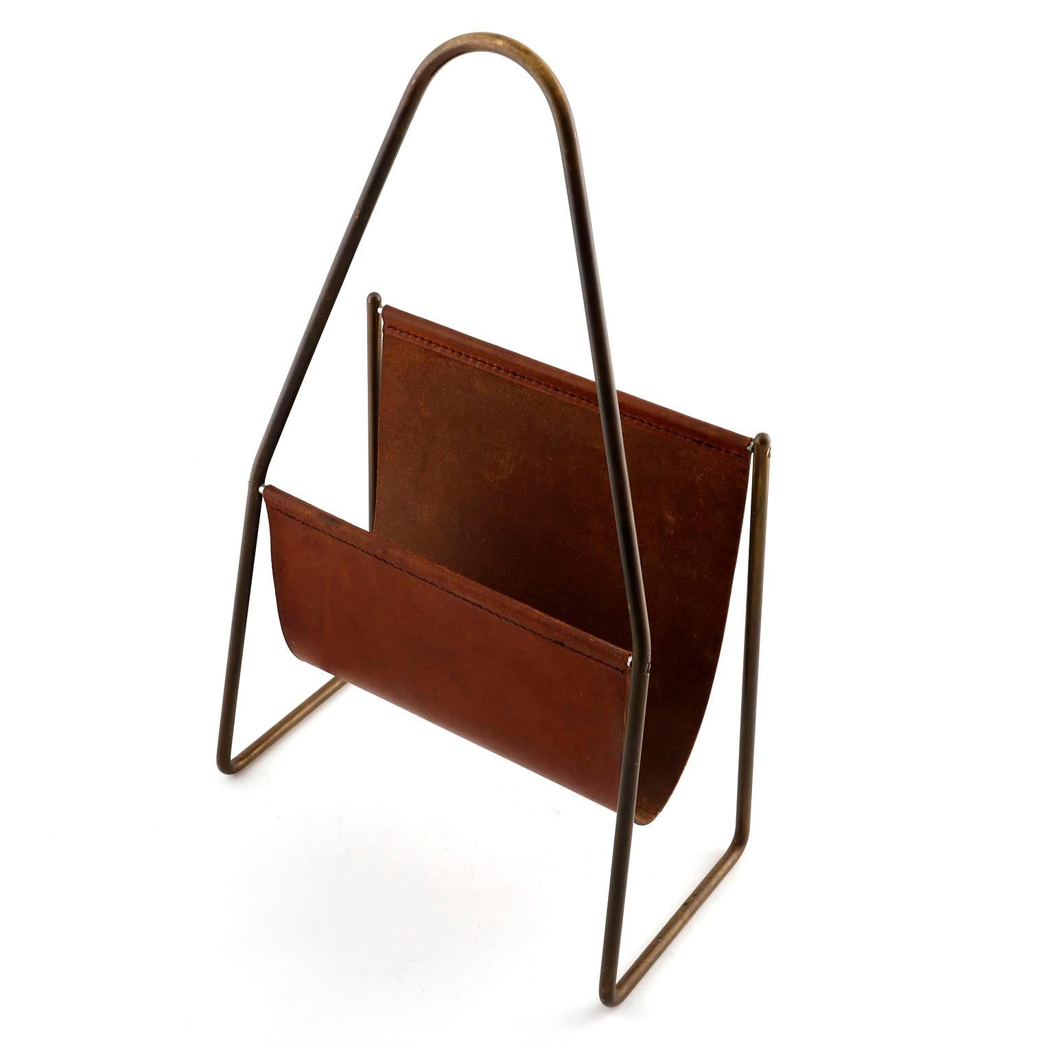 A magazine or newspaper tray made of patined brass and brown leather designed by Carl Auböck, manufactured by Carl Auböck workshop in midcentury, circa 1950, Vienna, 1950s. 
An authentic handmade piece in very good original condition with nice and