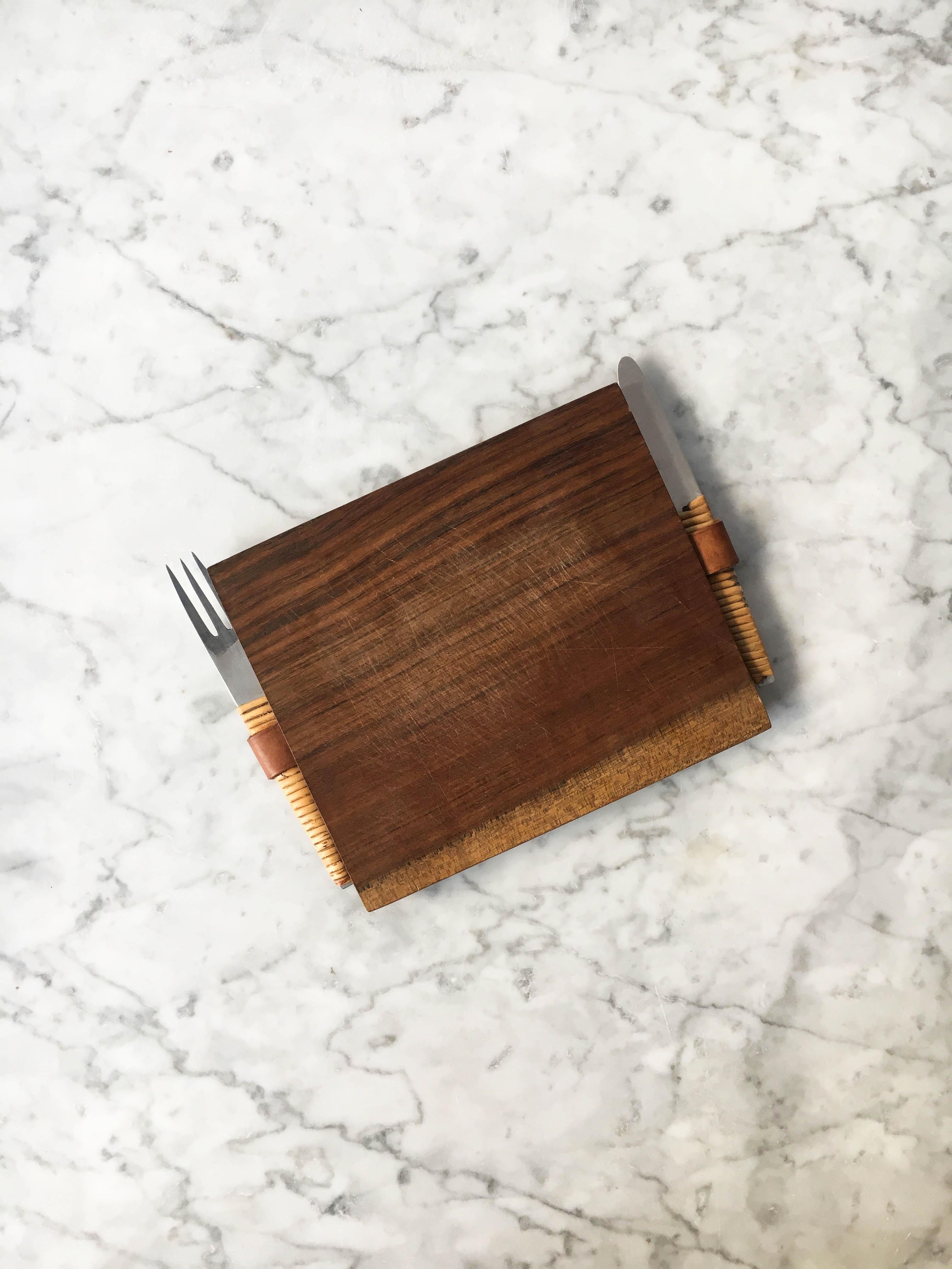 Splendid vintage picnic board with knife and fork, Austria, 1950s. The wooden cutting board has a trapezoidal shape with a leather loop, holding a cane-wrapped stainless steel knife and fork. In excellent condition with just the right amount of