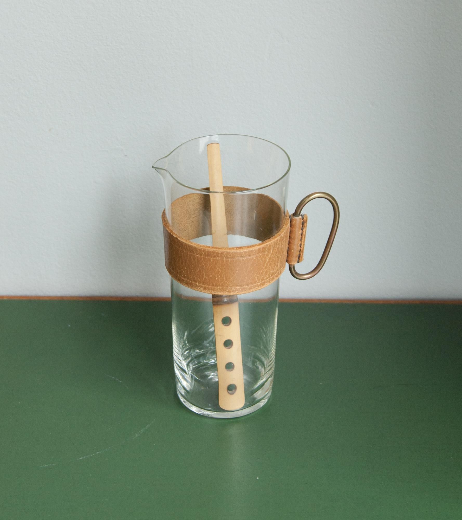 A glass pitcher with leather sleeve handle by Carl Auböck II, Vienna, 1950s.
A brass handle is attached to the leather sleeve and a drink stirrer in bamboo with four circular holes comes with the set. In excellent condition.