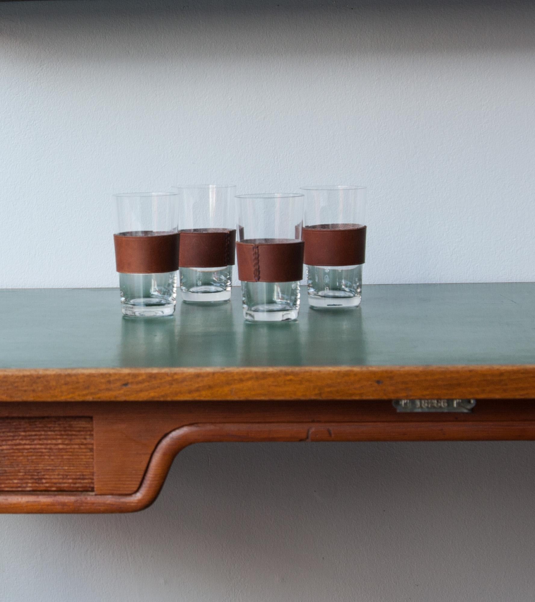 A set of four glasses with leather handle by Carl Auböck II, Vienna, circa 1950s.
The leather handles have a rich dark brown colour and are hand stitched around the glasses with a black stitching. A simple and elegant design from the Auböck