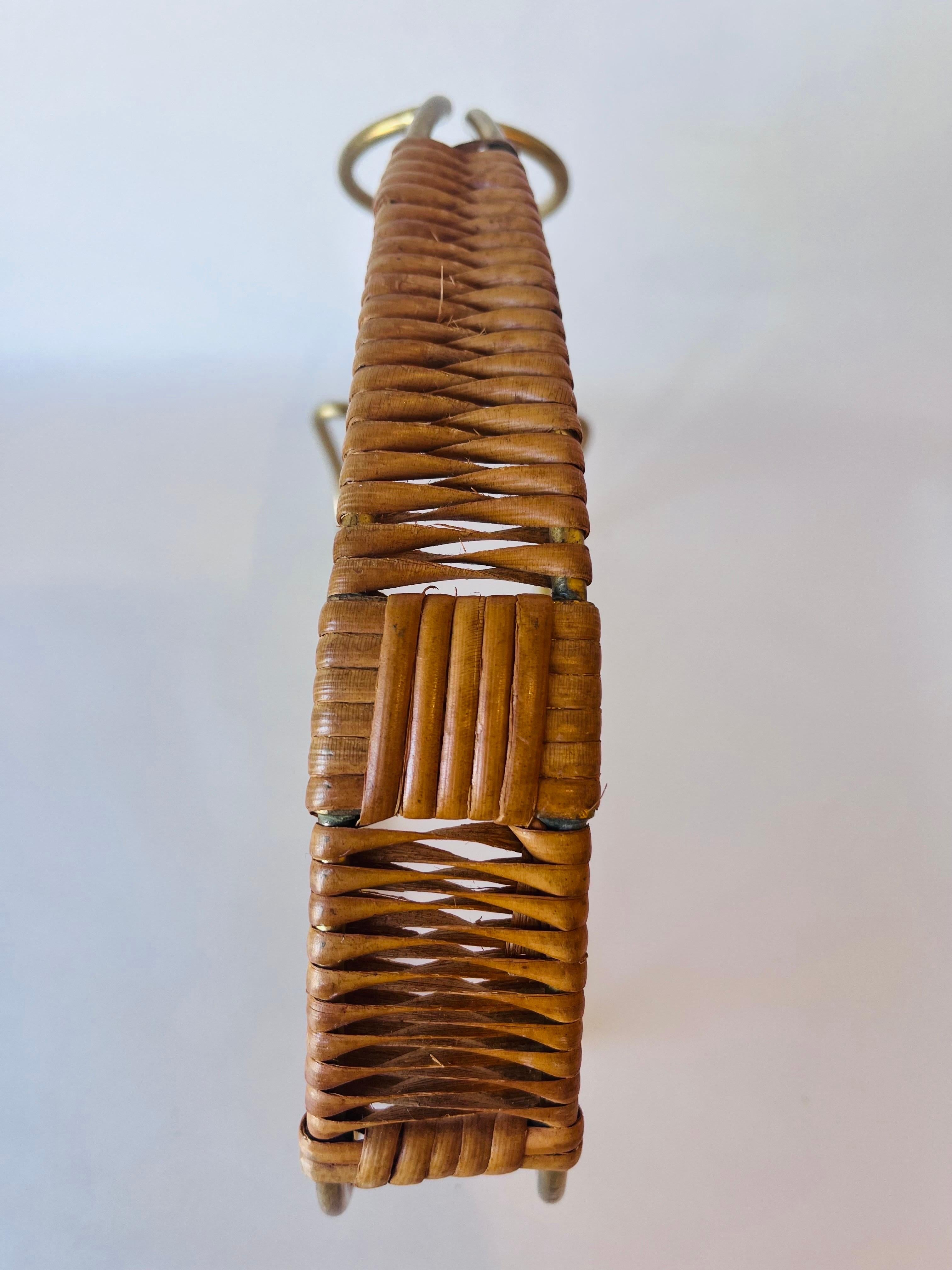 A vintage, mid century brass and woven rattan wine bottle holder / decanter designed in the style of Carl Aubock. In vintage condition with a beautiful patina with the requisite nicks and marks indicating a life well lived and loved to this brass