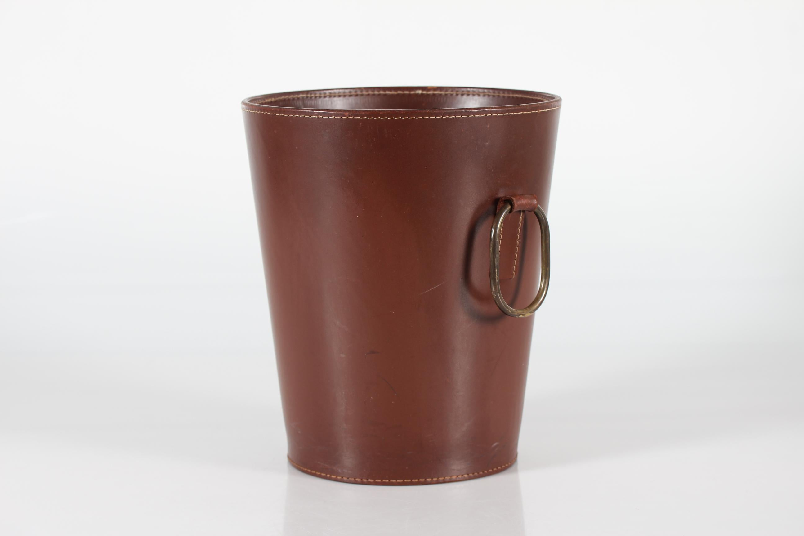 Round European vintage wastepaper basket from the 1970´s by Carl Auböck made for Illums Bolighus in Copenhagen.
It's made of strong genuine dark brown cognac colored core leather with visible stitching and ring shaped handle of brass.
It remains in
