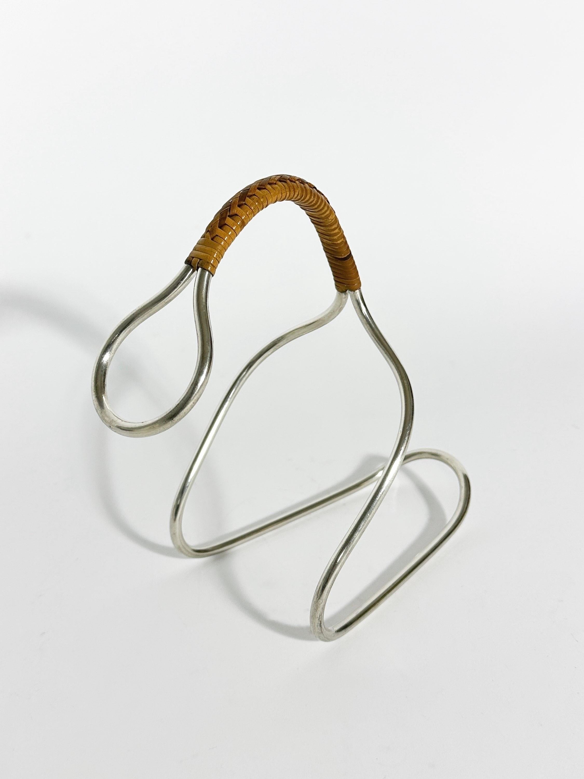 Carl Auböck bottle holder in a rarely seen nickel silver version, made in Vienna in the 1950s. 

Nickel silver with a hand-woven wicker handle. Cleaned and polished.

Width: 22 cm
Depth: 10.5 cm
Height: 20 cm