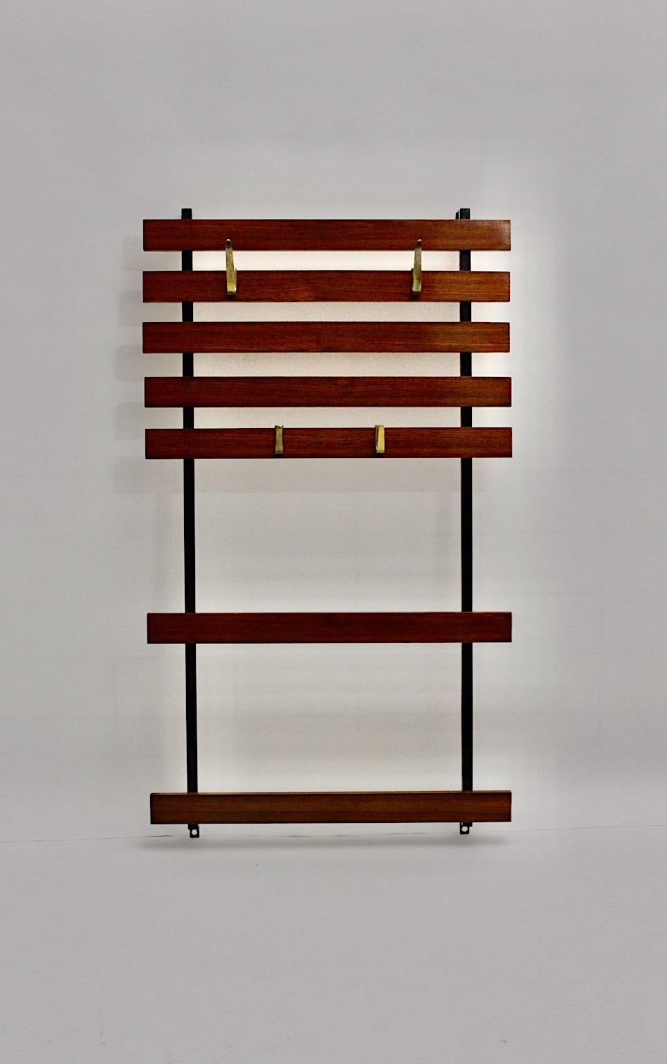 Mid-Century Modern vintage walnut coat rack with 4 cast solid brass hooks, which was designed and manufactured in Vienna, Austria.
The black lacquered metal frame shows 7 hardwood stained slats, which is provided for wall mounting, while the 4 cast