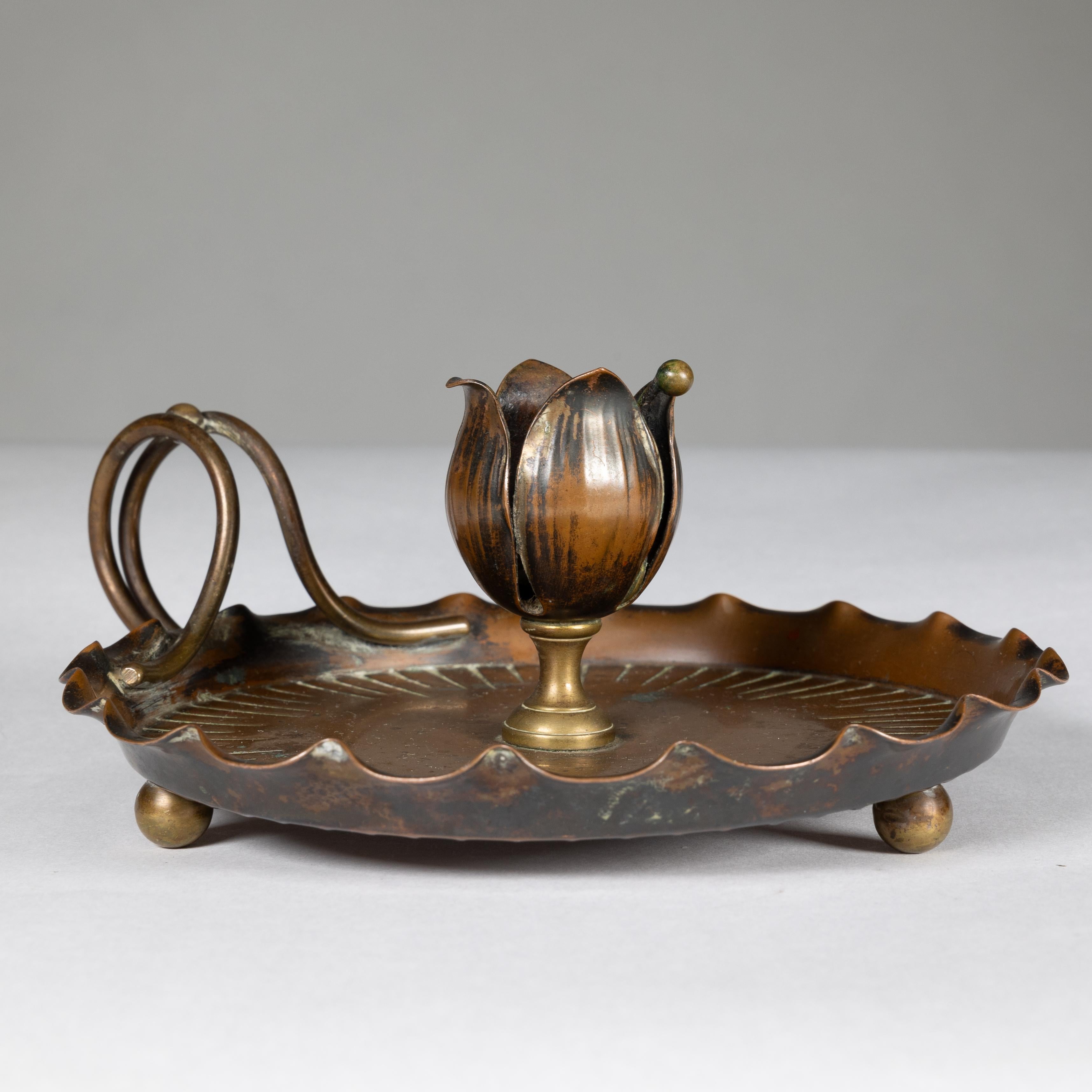 Carl Deffner. Esslingen. Allemagne. Bougeoir en cuivre de style Arts & Crafts avec un seul bouton de fleur composé de quatre feuilles, une base ondulée, une double poignée circulaire et des pieds en forme de boule à la base. Marque de fabrique sur