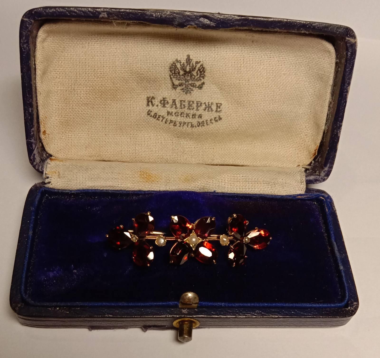 A collectible gold Carl Faberge brooch with 10 garnets, 3 pearls and 2 marcasites. In its original case of the Moscow branch of the Faberge company, circa 1908-1915. 

Brooch size: 40/11/10 mm. Case size: 82/42/25 mm. 

Weight: 4.68 grams, 56