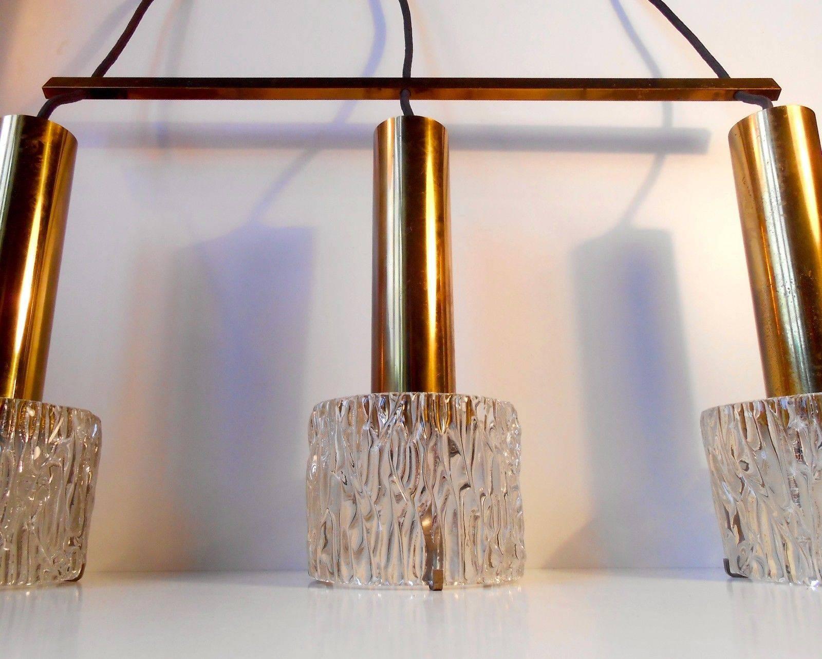 Three-shaded height adjustable ceiling light in solid patinated brass and heavy crystal glass. It was designed by Carl Fagerlund for Orrefors in Sweden during the 1950s. The light is in original, vintage and working condition. There will be
