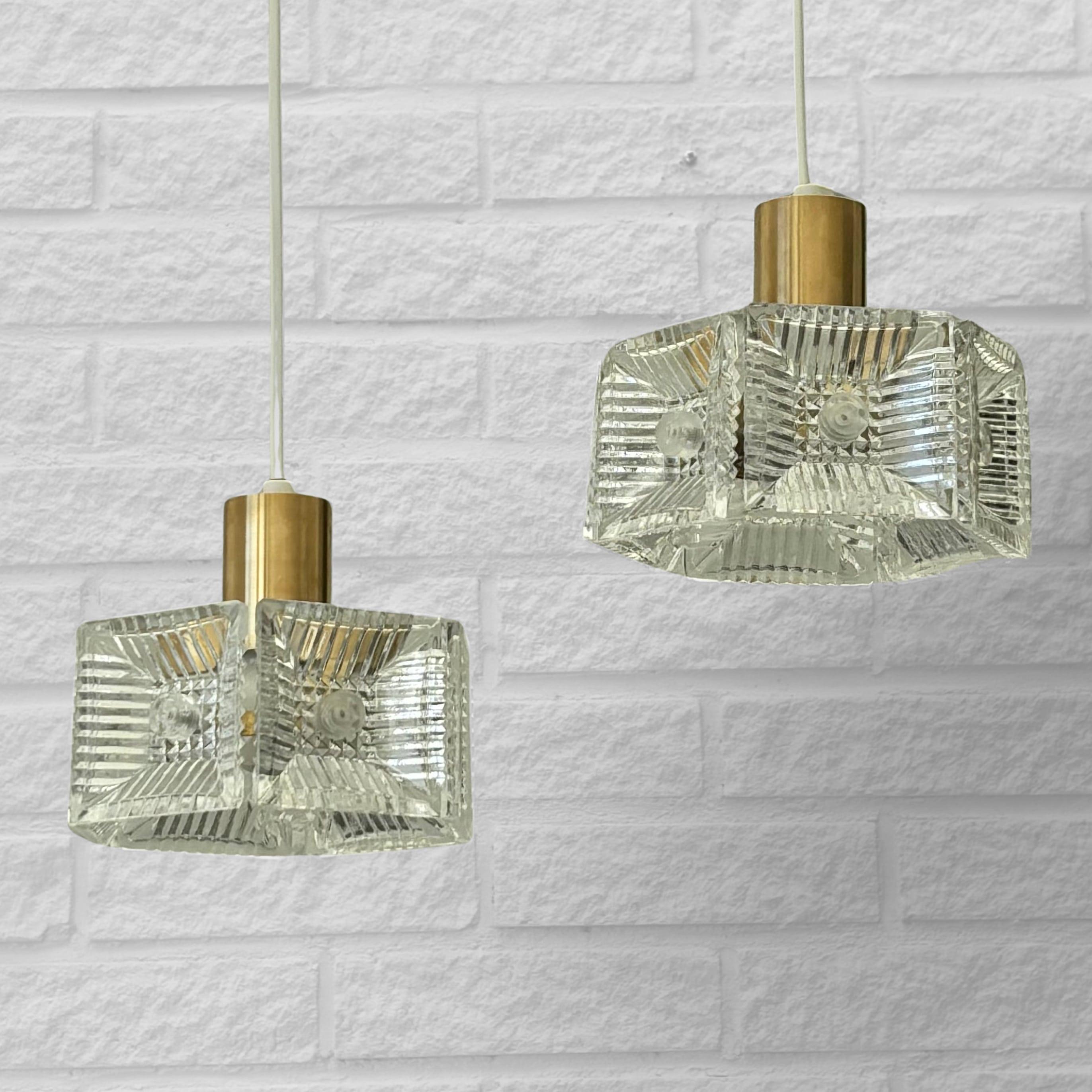 A pair of Mid-Century Modern pendant lamps designed by Carl Fagerlund for the Swedish glassworks Orrefors in the 1960s. Crafted from brass, each lamp features six square glass prisms.

The glassworks Orrefors was founded in 1897 and soon became one