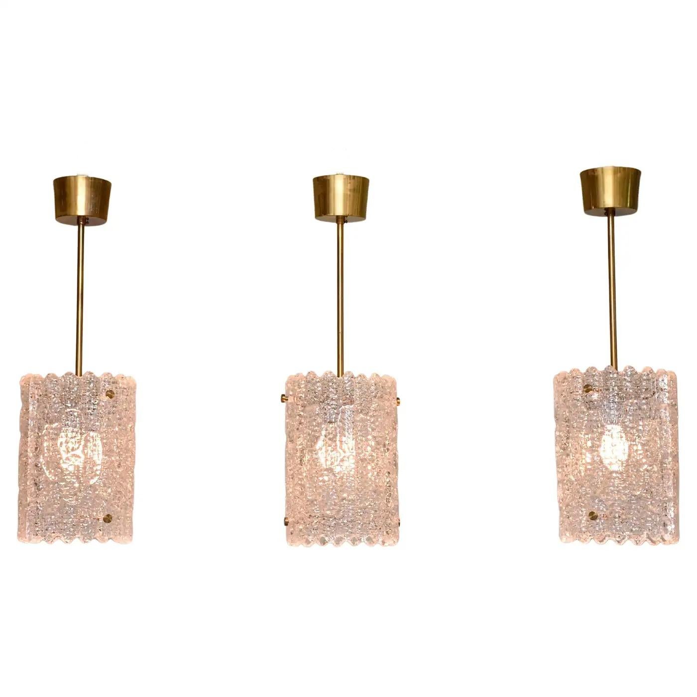 Lampade a sospensione cilindriche degli anni '60 di Carl Fagerlund per Orrefors, Svezia, ciascuna composta da due pannelli curvi di spesso vetro testurizzato collegati da aste di ottone massiccio. 
La caduta totale, compresa la coppa del baldacchino