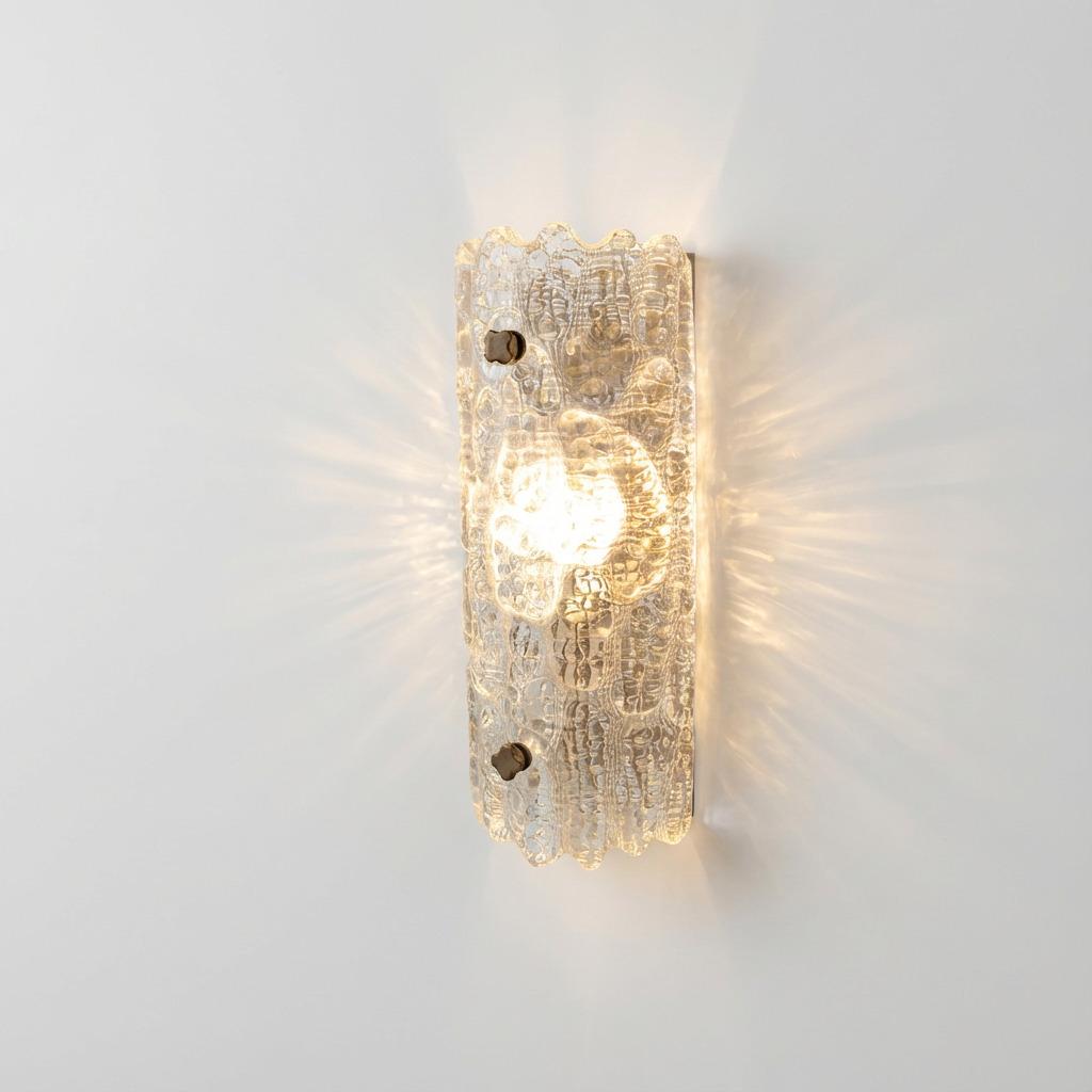 Aplique de pared diseñado por Carl Fagerlund con pantalla de cristal transparente de textura gruesa con un marcado dibujo en relieve. Forma curva montada con pomos de sujeción oscuros visibles que fijan el cristal a la placa posterior. La superficie