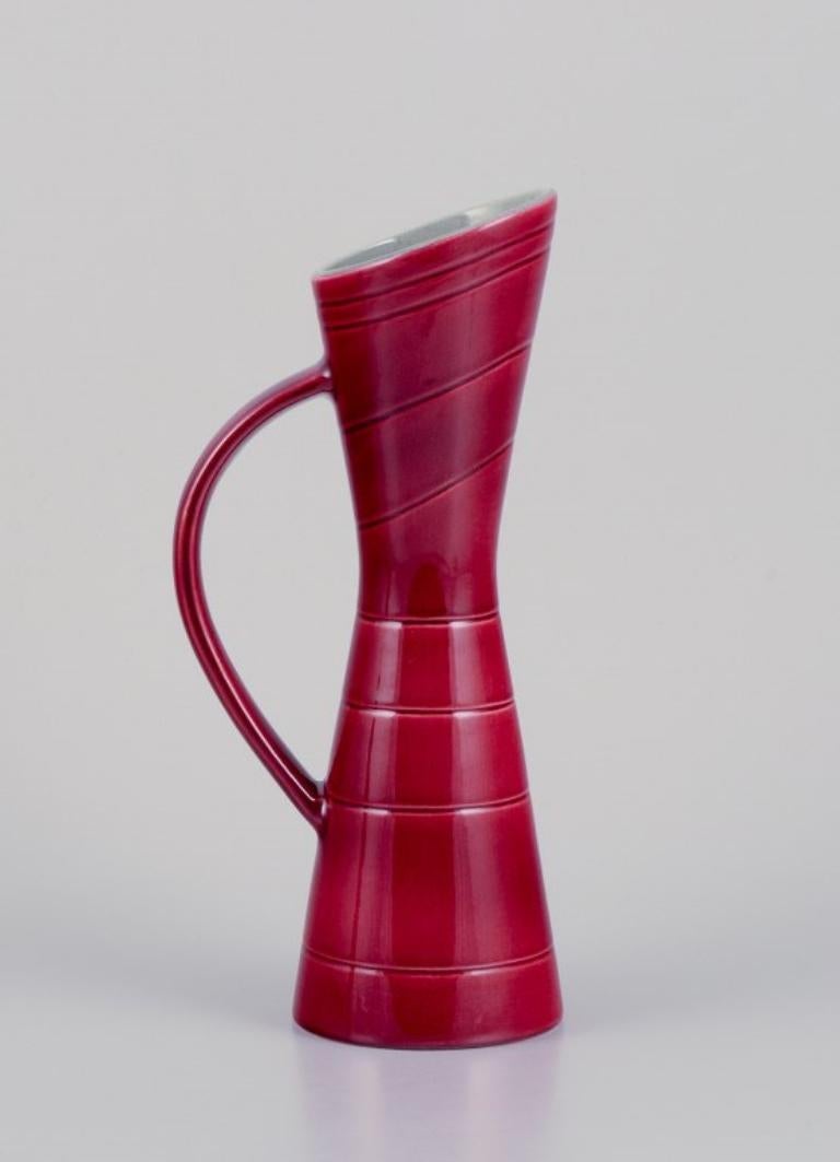 Carl Harry Stålhane (1920-1990) für Rörstrand. 
Zwei Krüge und ein Teller aus Keramik. Burgunderfarbene Glasur.
Aus der Reihe 