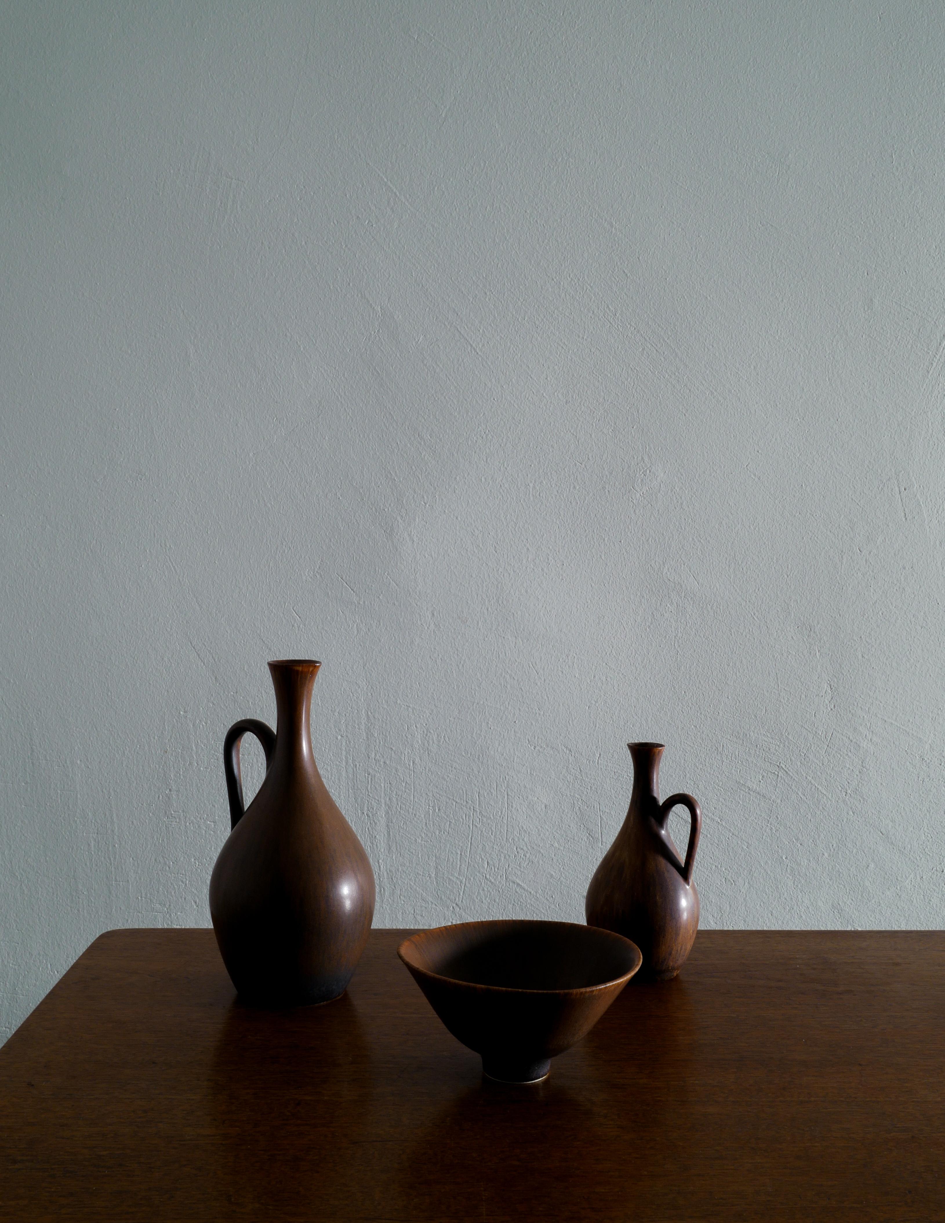 Rare set of ceramics by Carl-Harry Stålhane in a brown glaze produced by Rörstrand, Sweden in the 1950s. In good vintage and original condition with minimal signs of use. All signed. 

Dimensions: 
Larger pitcher: H: 23 cm Diameter: 11 cm 
Smaller
