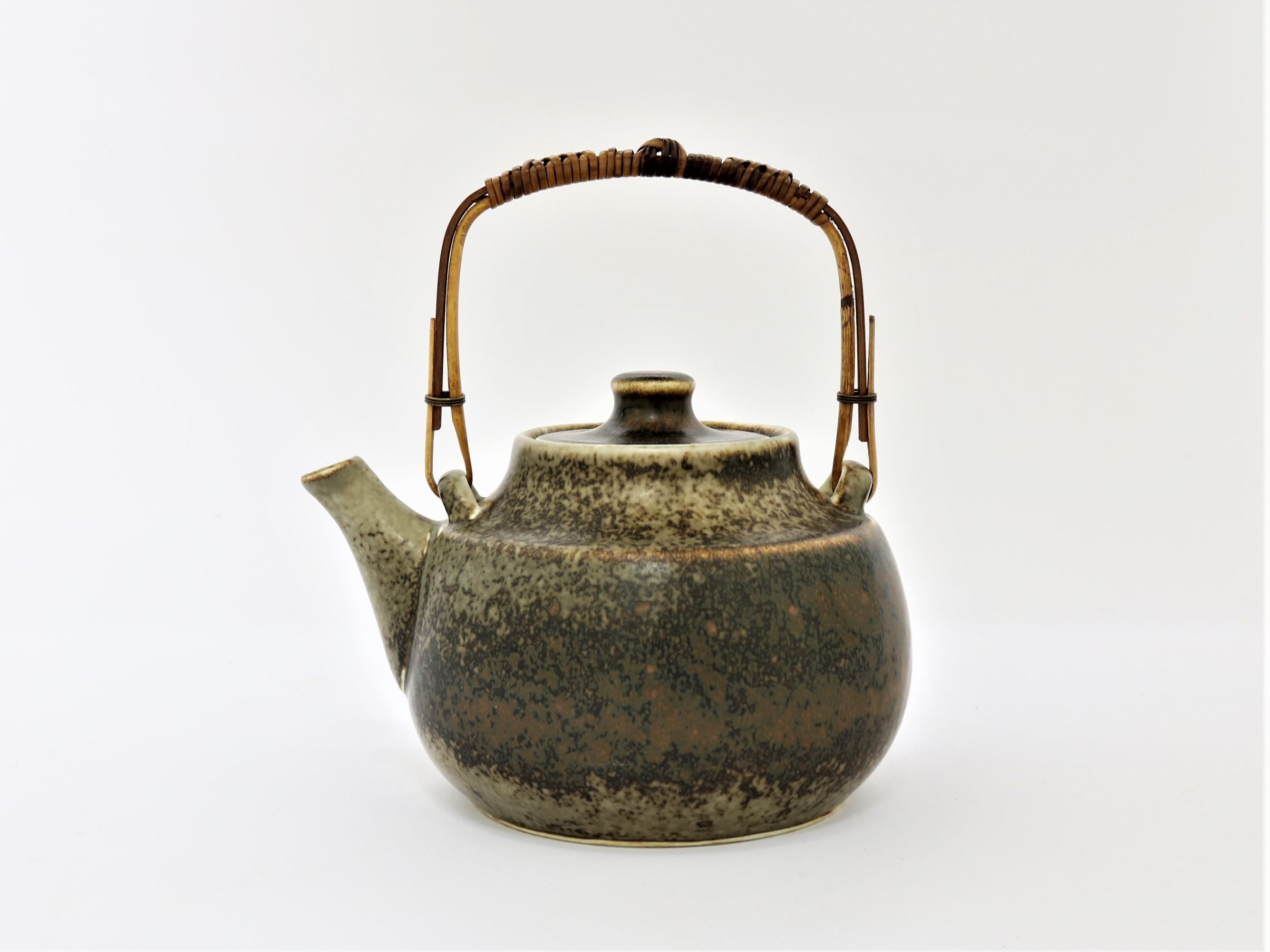 A large stoneware teapot with a bamboo handle covered with rattan and a semi matte speckled brown glaze by Carl-Harry Stalhane for Rorstrand in the 1960s.

Signed with artist signature 