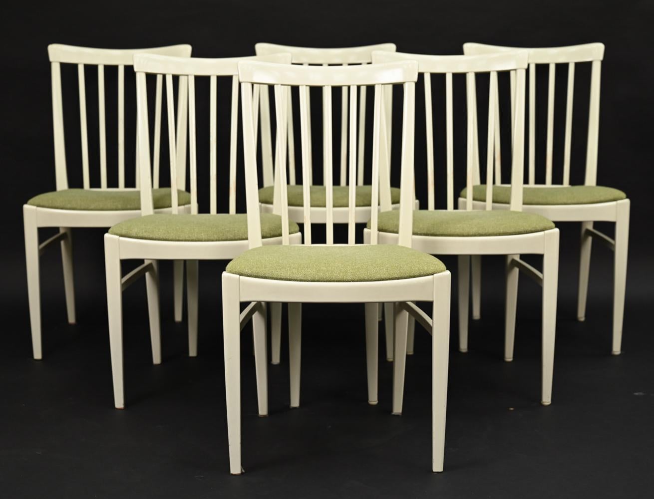 An elegant Swedish mid-century dining suite in the Gustavian style, in off-white painted beech wood. Comprised of a tall cabinet with interior fitted with shelving, (6) spindle back dining chairs with green wool seats, and dining table with leaf