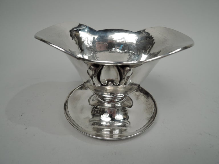 Danish Modern hand-hammered sterling silver sauce bowl on stand. Made by Carl Poul Petersen in Canada, ca 1940. Tapering ovoid bowl with flared ends and scalloped rim. Stylized leaf between buds applied to sides. Concave ovoid leaf between two buds