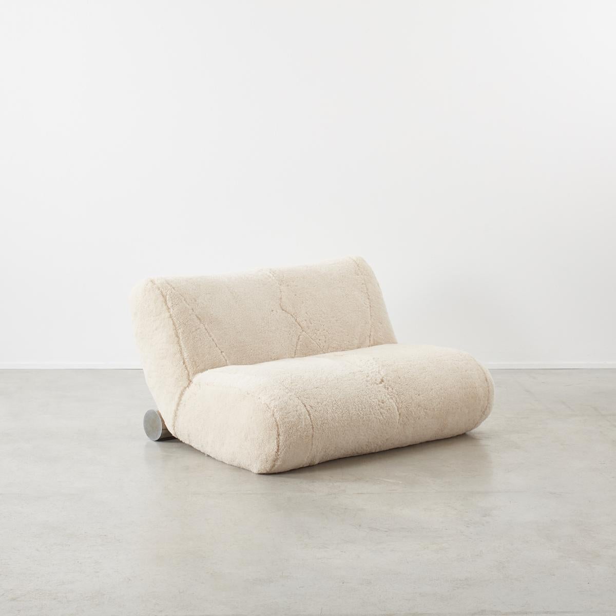 This minimal seventies loveseat has a simple curved side profile accented with a chromed cylinder base piece. This sofa is very soft and squishy offering the user an extremely comfortable seating experience. The sofa has been recently reupholstered