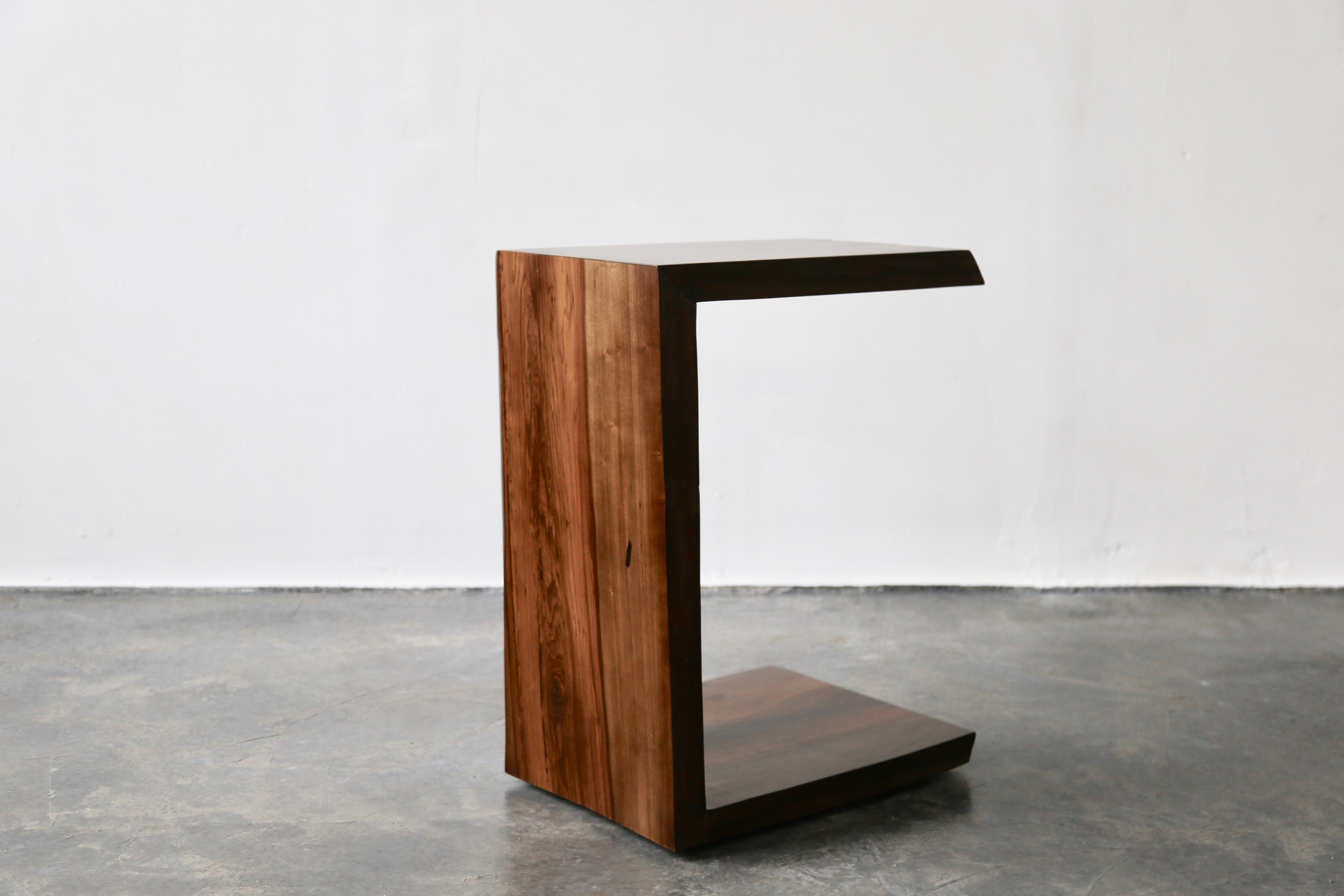 The Carlo table is a cantilevered occasional table, designed to slide under a sofa or sitting area as necessary, and fashioned from slabs of sustainable sourced solid Argentine rosewood. Shown here in a natural finish, it is customizable to your