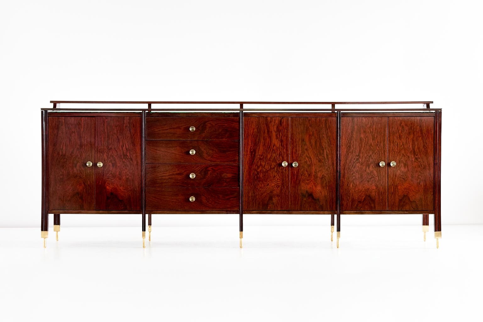 This rosewood sideboard/credenza was designed by Carlo de Carli and produced by Sormani in 1964. The large sideboard is executed in a combination of solid and veneered rosewood. The particularly striking brass feet and handles give the piece a light