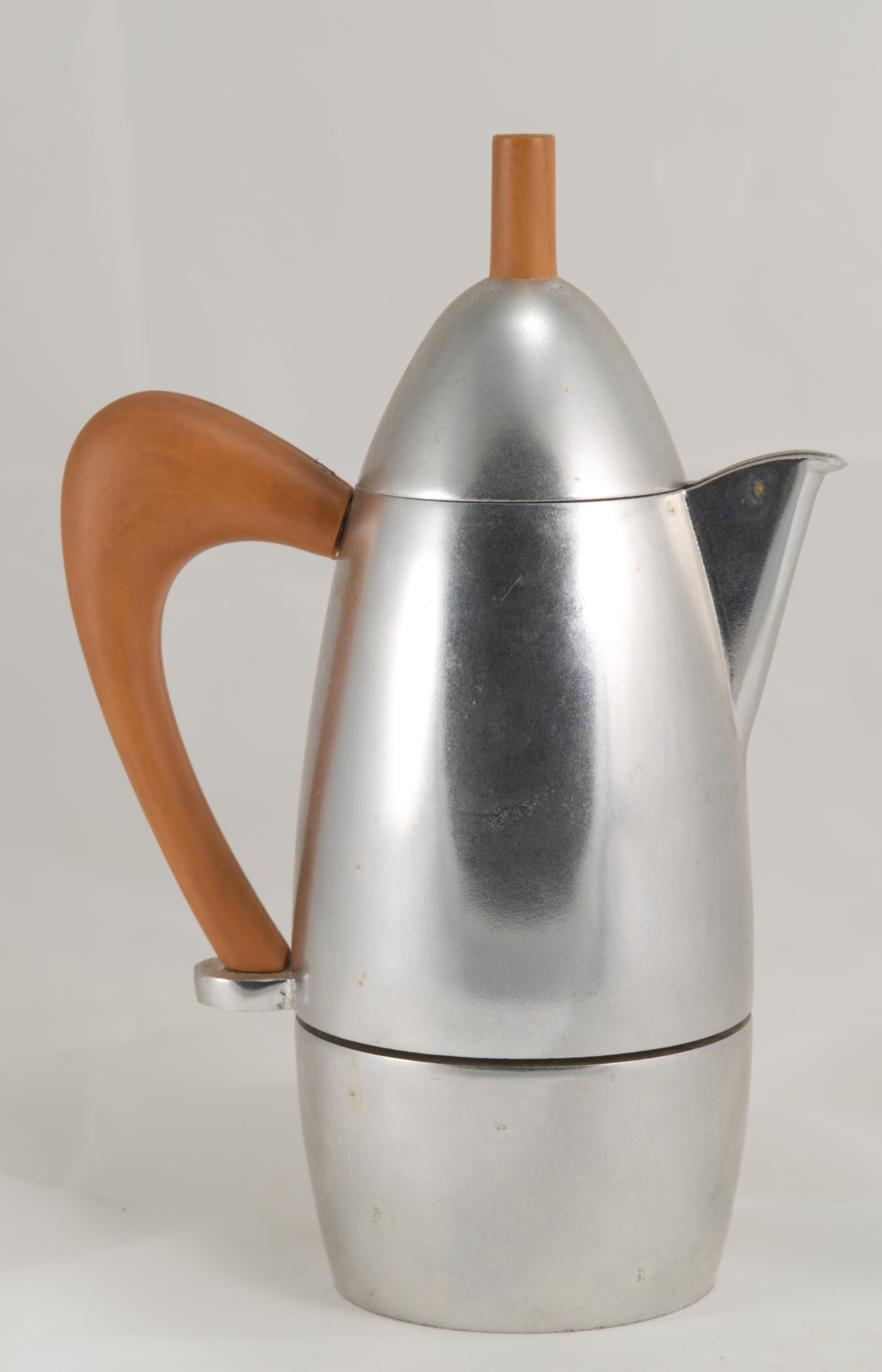 La Carlo Giannini Chicca Caffettiera, ou cafetière Espresso, présente un design moderniste avec un corps en forme d'ogive et une poignée angulaire, réalisés en fonte d'aluminium et en faux bois. La cafetière a été conçue par le Studio Carlo Giannini