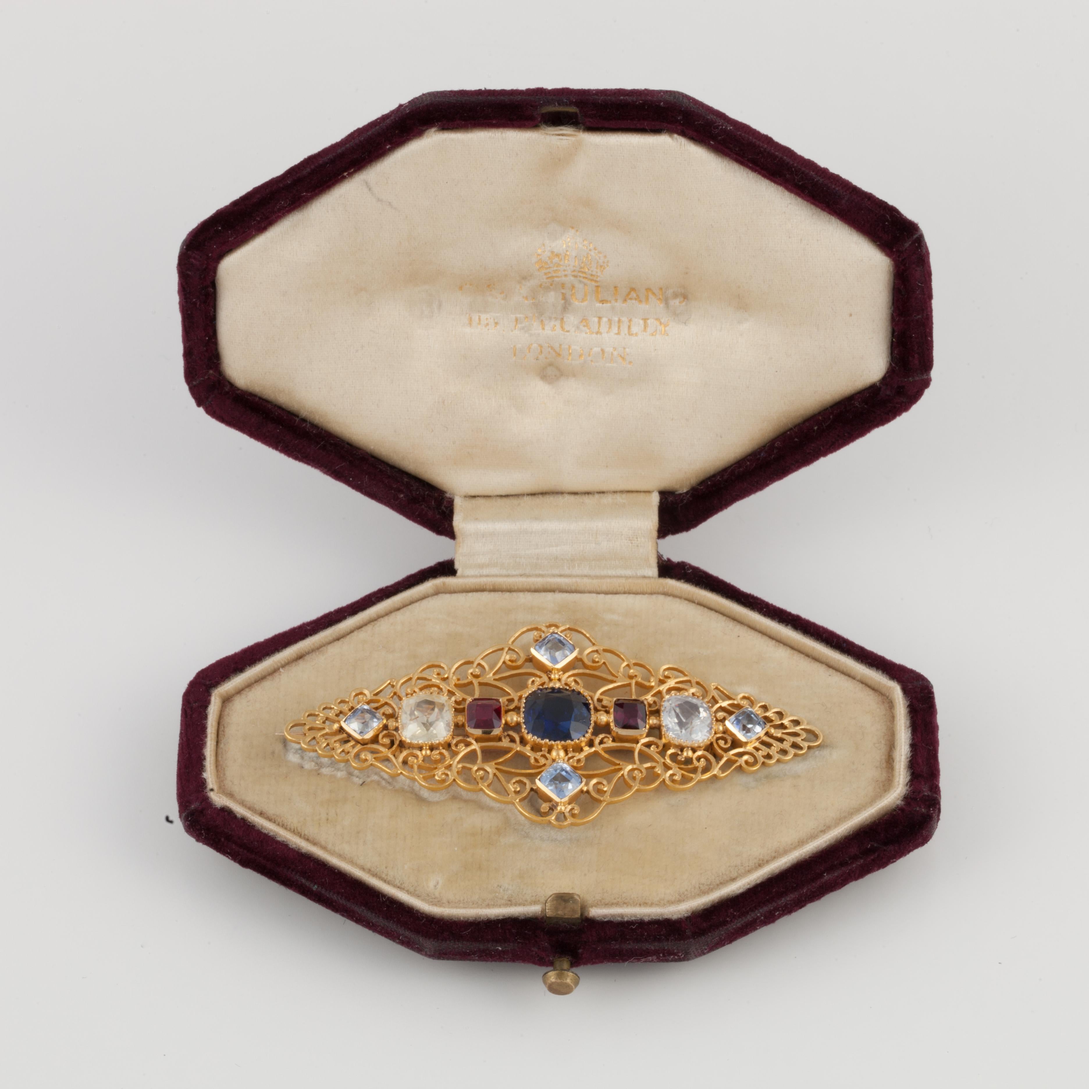 Victorian Carlo Giuliano 18K yellow gold sapphire and ruby pin featuring his signature gold open-work. The pin contains two rubies that total 0.70 carats, no treatment, Thailand origin, accompanied by a GIA report.  There are seven multi-colored