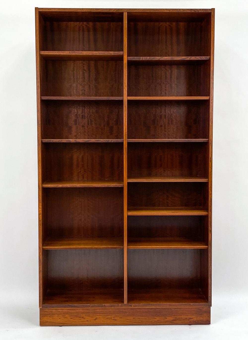A handsome Danish mid-century double bookcase in fine rosewood veneer, designed by Carlo Jensen for Poul Hundevad, c. 1960's. This beautiful piece features two sides of adjustable shelves in a sturdy, minimalist form to blend seamlessly into any