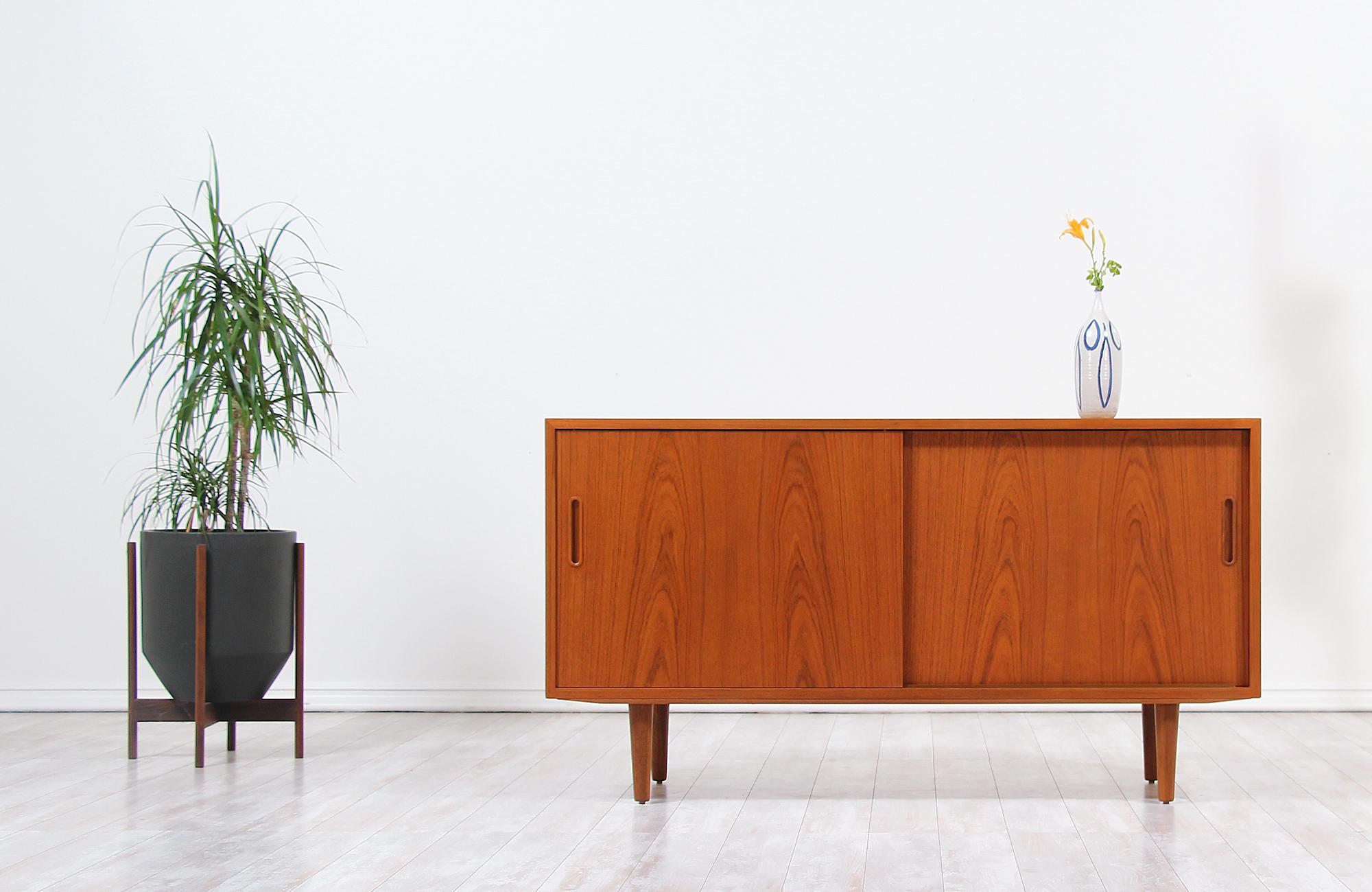Compact Danish modern credenza designed by Carlo Jensen for Hundevad Co. in Denmark, circa 1960s. This compact credenza features a solid teak wood case with a birch wood interior and two doors that open smoothly revealing ample storage space. The