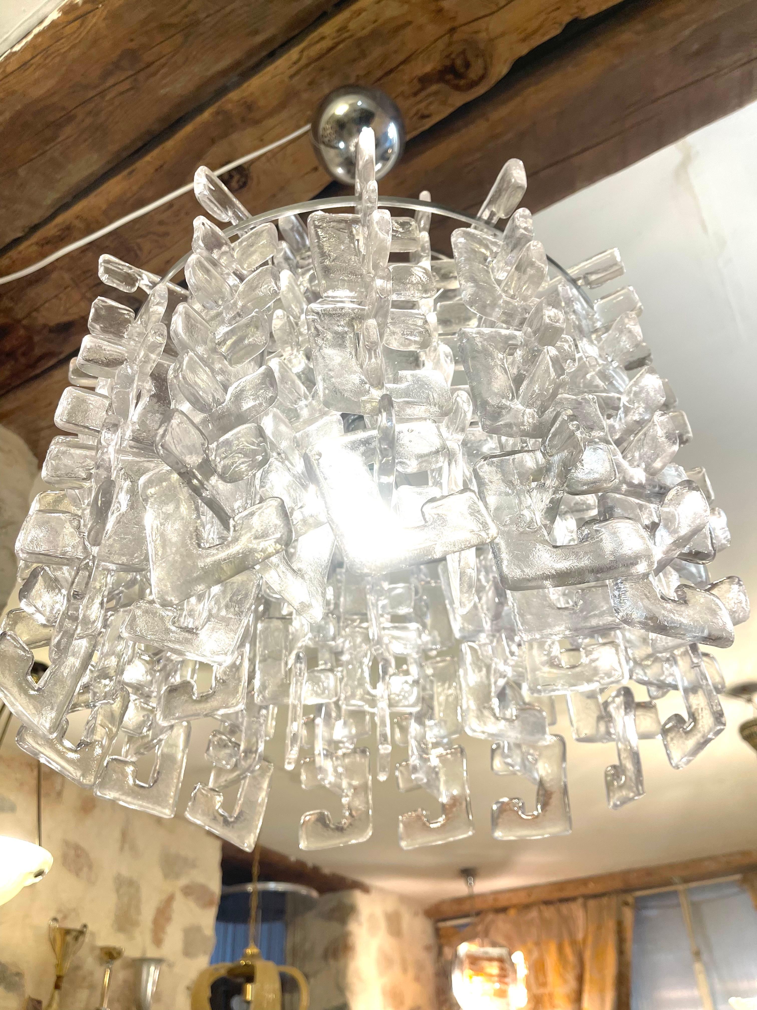 Lampadario di Carlo Nason per Mazzega, 1960
Un lampadario vintage che racchiude la tendenza di metà secolo di sospendere più elementi da una struttura.
Carlo Nason ha adottato questo concetto con elementi a incastro che consentono di ottenere