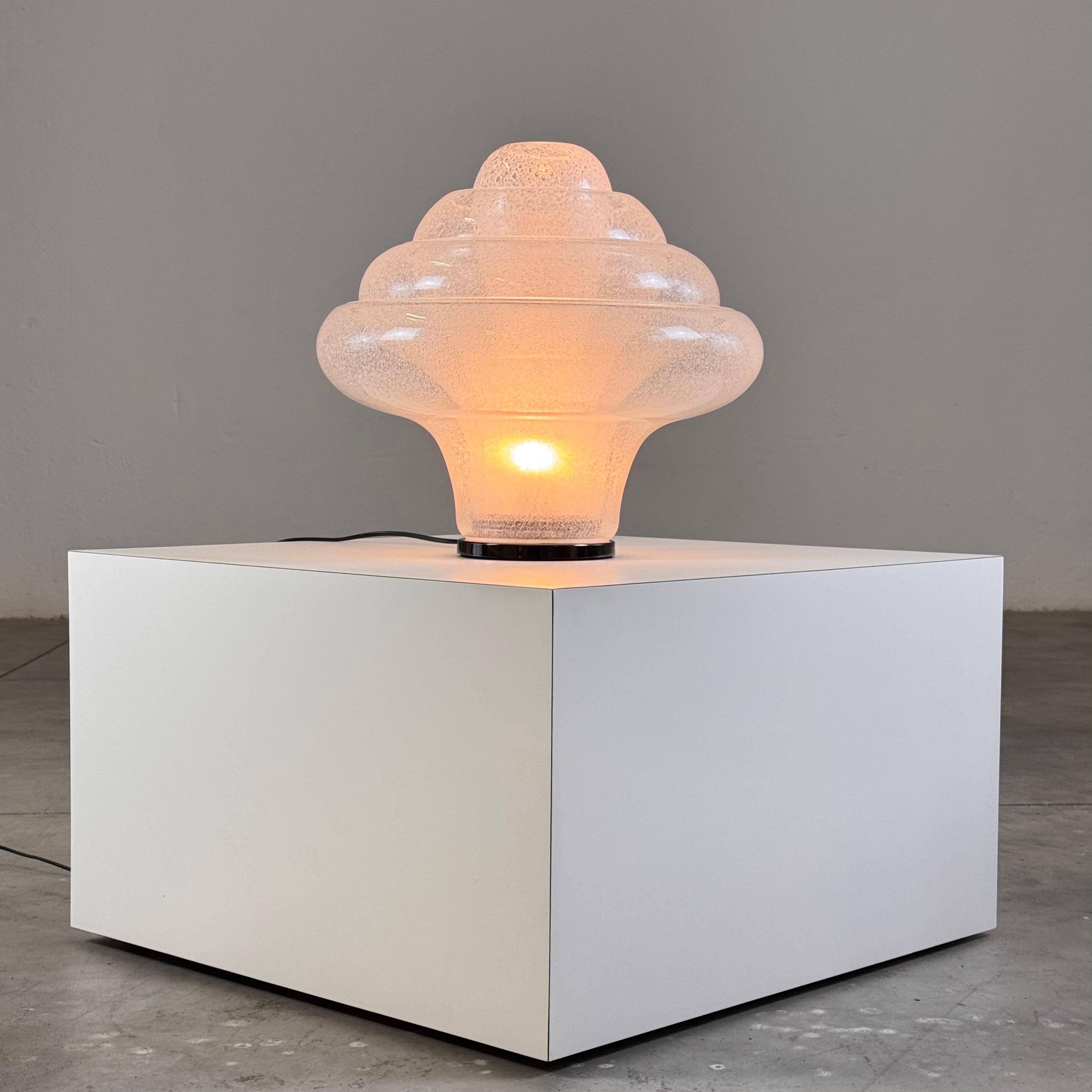 The LT305 'Lotus' table lamp, designed by Carlo Nason for Mazzega in the 1960s, epitomizes Italian craftsmanship and artistic innovation. This particular piece, produced in the late 1990s, features stunning Pulegoso glass, renowned for its unique