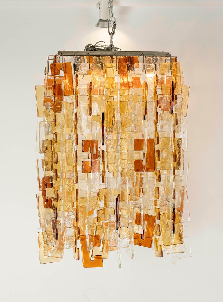 Italian Mid-Century Modern multicolored interlocking murano glass chandelier on chrome base by Carlo Nason for Mazzega. This stunning Murano chandelier is comprised of clear, gold and amber glass. Chandelier can be suspended from a chain with choice