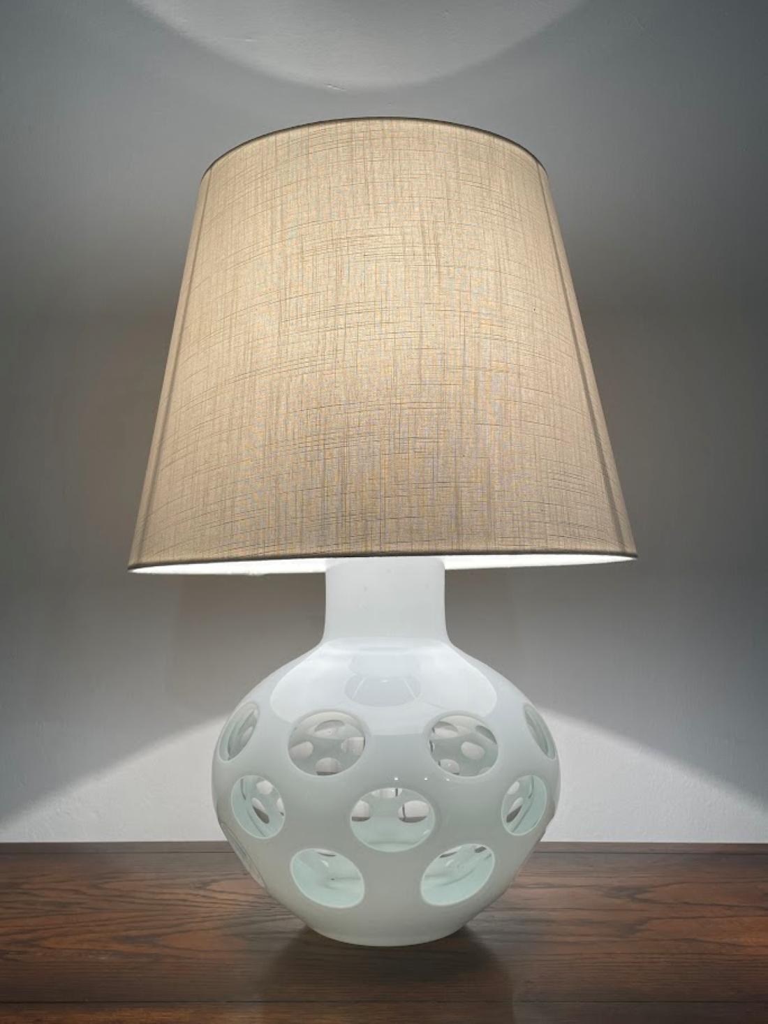 
Découvrez la lampe de table conçue par Carlo Nason pour Mazzega, une harmonie parfaite entre l'art du verre de Murano et le design moderne.

La lampe présente une élégante base en verre de forme ronde, décorée de cercles translucides sur fond