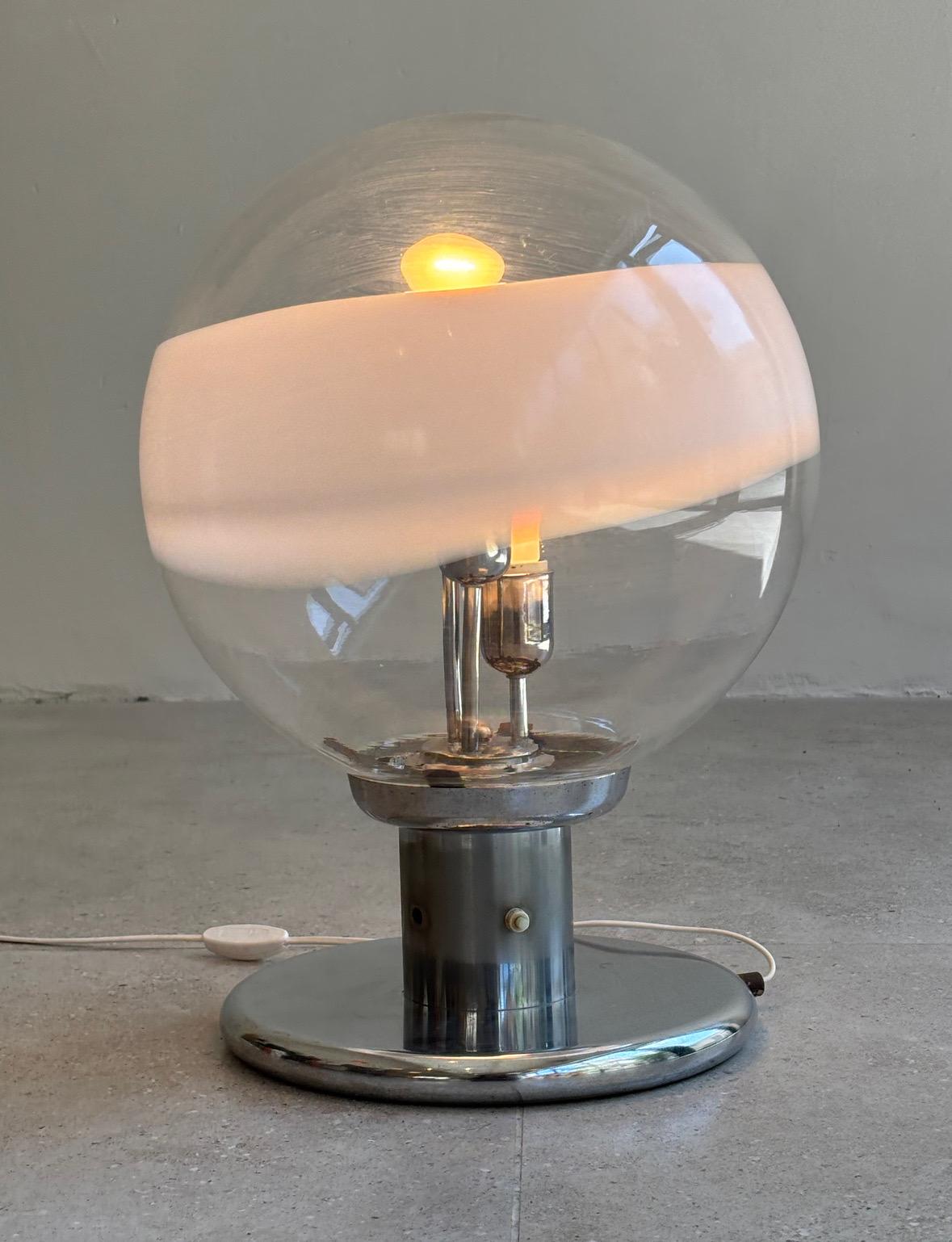 Esta llamativa lámpara de Carlo Nason, fabricada para Mazzega en Italia en la década de 1960, ejemplifica la atrevida elegancia del movimiento moderno Space Age. Presenta una esfera de cristal de Murano soplado a mano, cuyas gruesas paredes