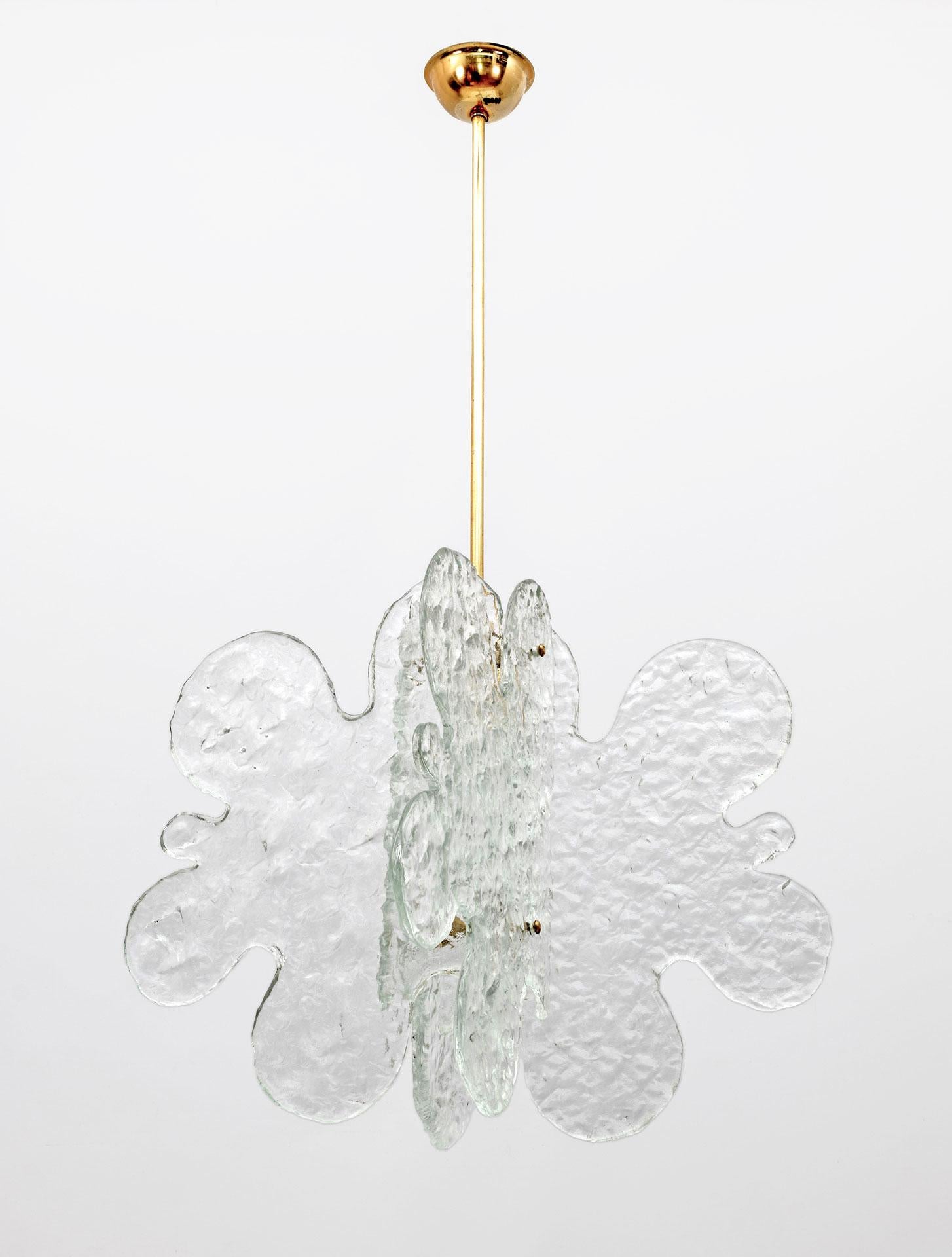 Murano glass chandelier designed by Carlo Nason and made by Mazzega in the 1970s characterized by four cloud-shaped and structured glass sheets joined by a central brass frame. The length of the stem can be adjusted as needed.
The suspension is