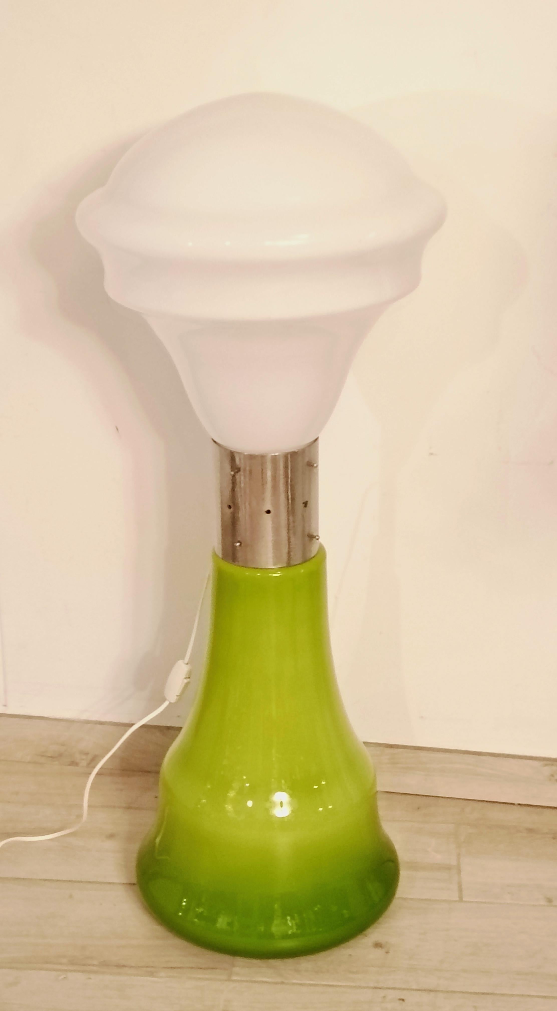 Elegante lampada da terra disegnata da Carlo Nason, caratterizzata da un design iconico e ricercato. La base è realizzata in vetro di Murano soffiato a mano, con una tonalità verde brillante che sfuma delicatamente verso il basso, donando un tocco