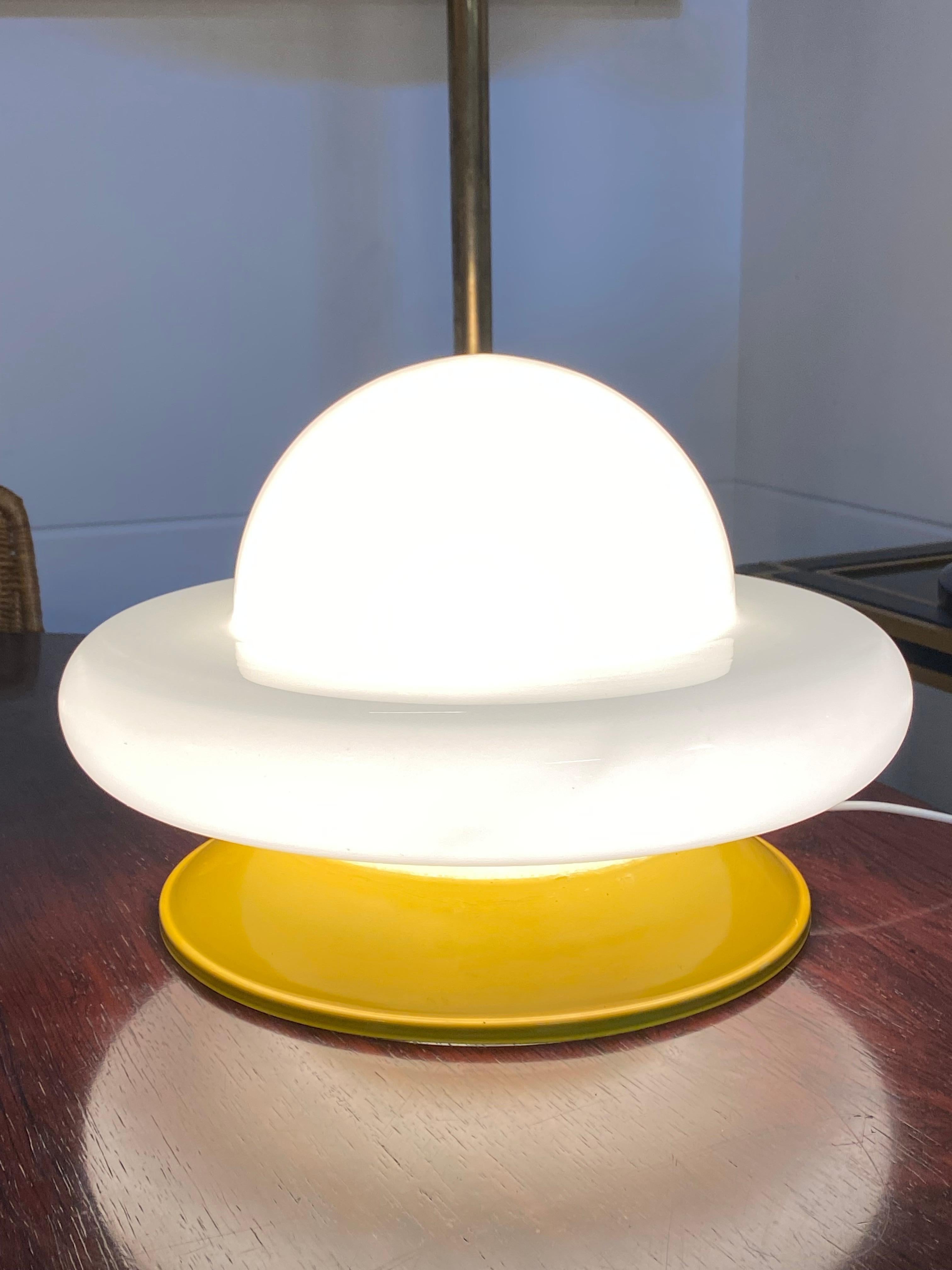 A round base in orange painted metal, a slim chrome stand and a semi-circular shade in opaline glass form this Space Age table lamp. The on/off button is located along the wire.
