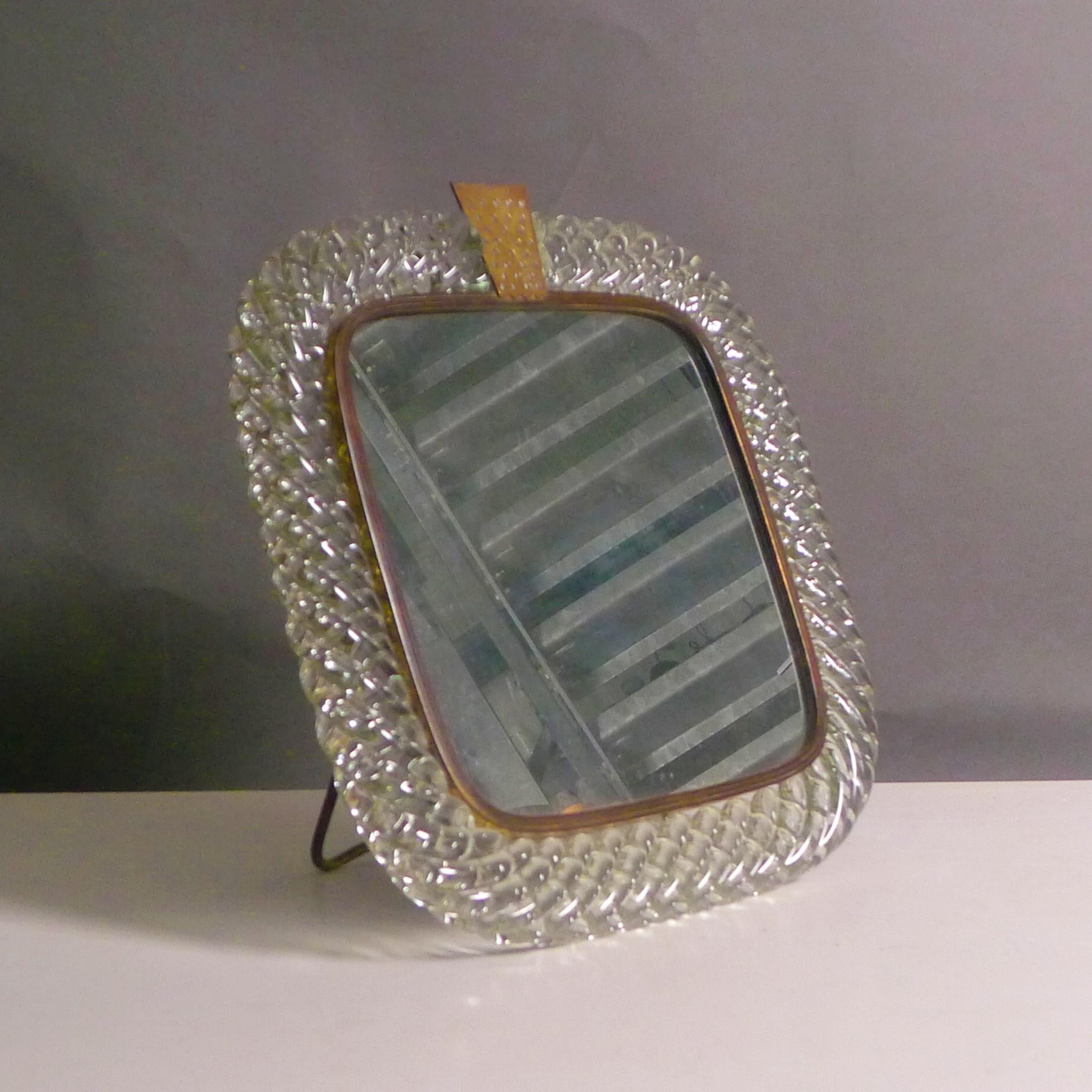 Carlo Scarpa (1906-1978)

Art Deco Glass Table Mirror

handworked in twisted colourless Murano glass, the spiral design known as “a treccia” after its resemblance to a braid.

The glass frame lined with a brass band, secured with a pierced trapezoid