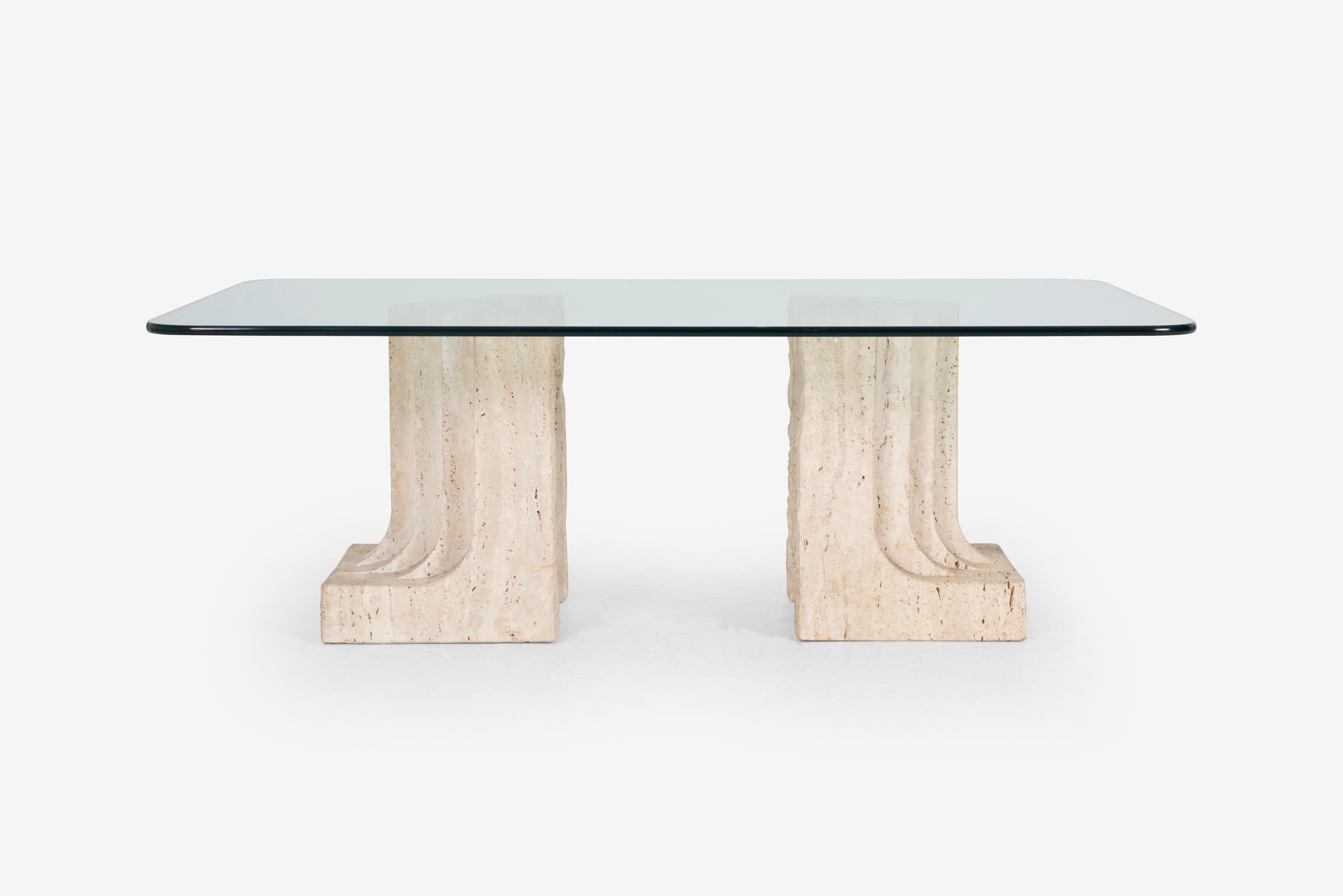 The coffee table is anchored by two robust, sculptural blocks of travertine. Exhibiting raw textures and subtle tonal nuances, the travertine blocks are reminiscent of the iconic Brutalist aesthetic, while their undulating forms evoke an organic