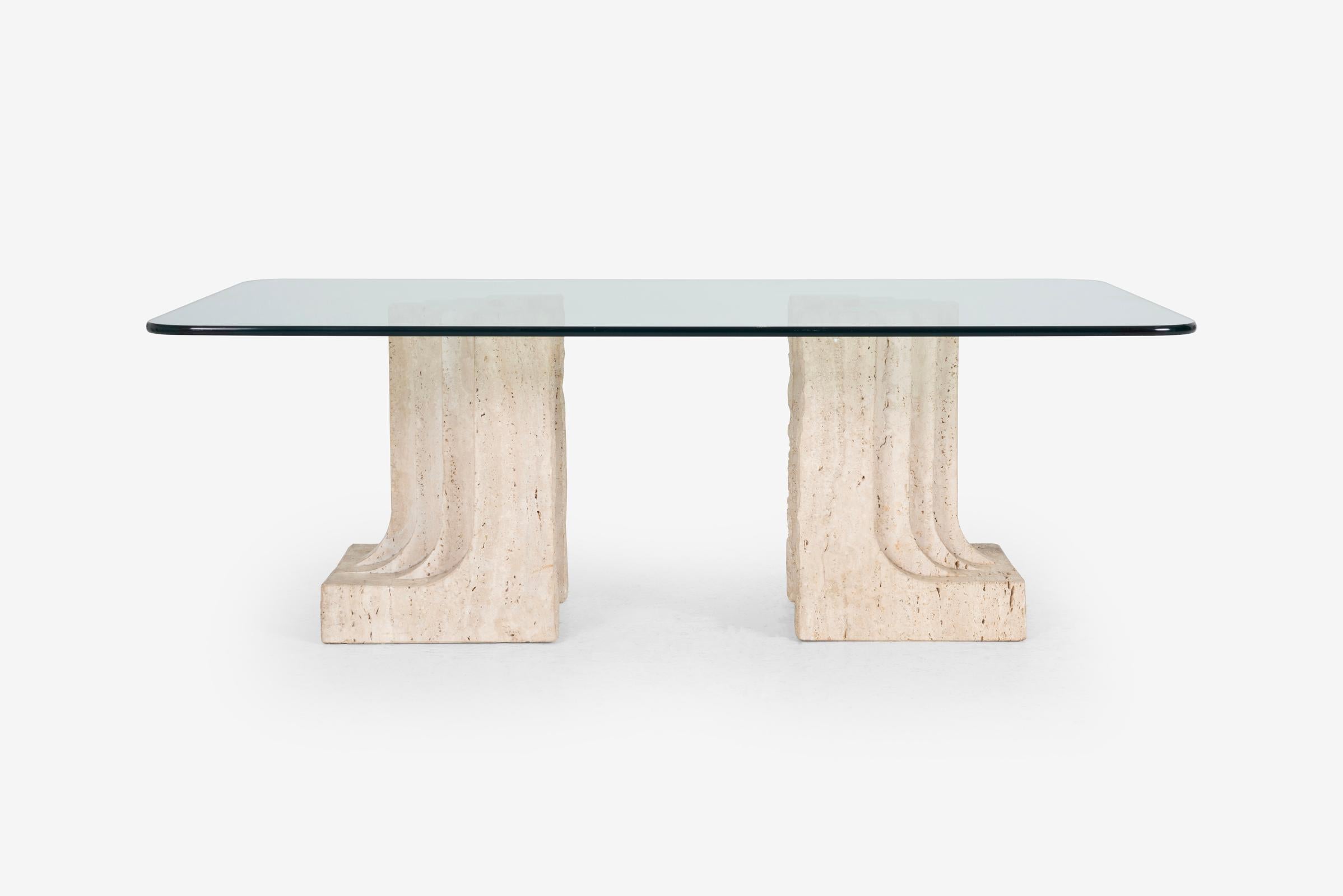 La table basse est ancrée par deux blocs de travertin robustes et sculpturaux. Présentant des textures brutes et des nuances tonales subtiles, les blocs de travertin rappellent l'esthétique emblématique du Brutalisme, tandis que leurs formes