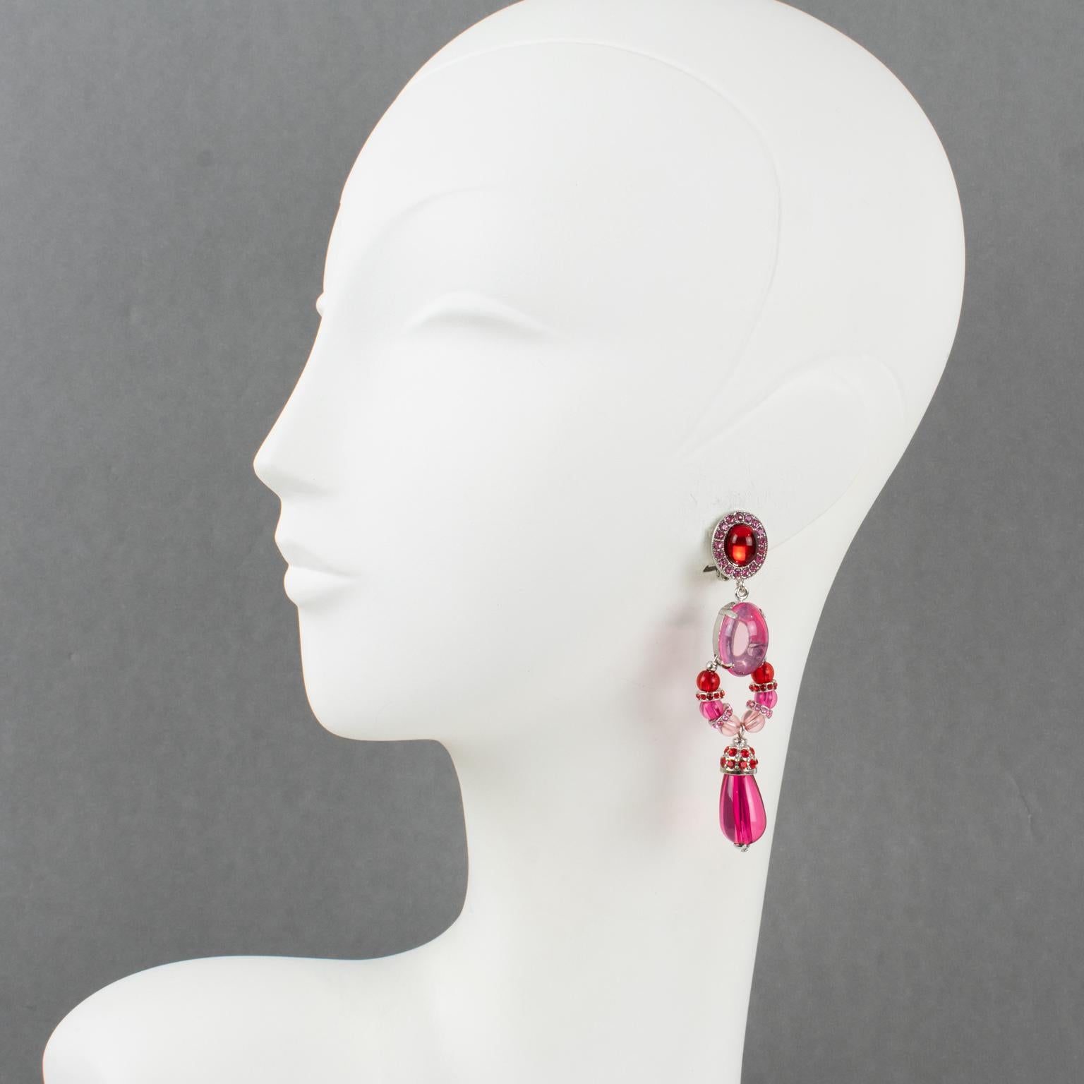 These sophisticated Carlo Zini dangling clip-on earrings feature a long geometric shape with silvered metal framing ornate with red, hot pink, and powder pink resin rhinestones and cabochons with dangle teardrop beads. They are marked at the back