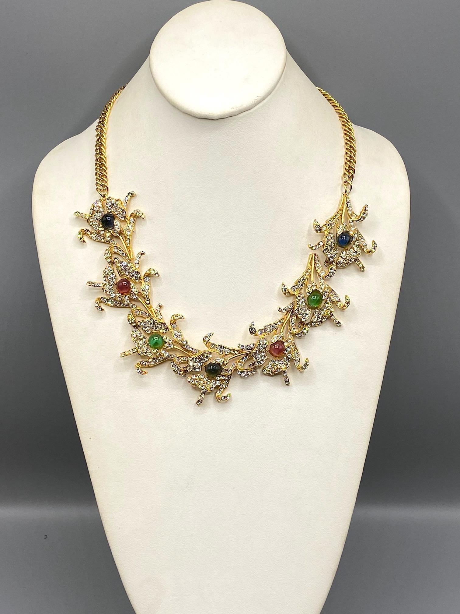 Presented is an eye catching creation by Carlo Zini of Milan, Italy. The design is a lovely composition of seven pansy flowers linked together and suspended from a chain. Each flower features a central glass cabochon in red, blue or green. The glass