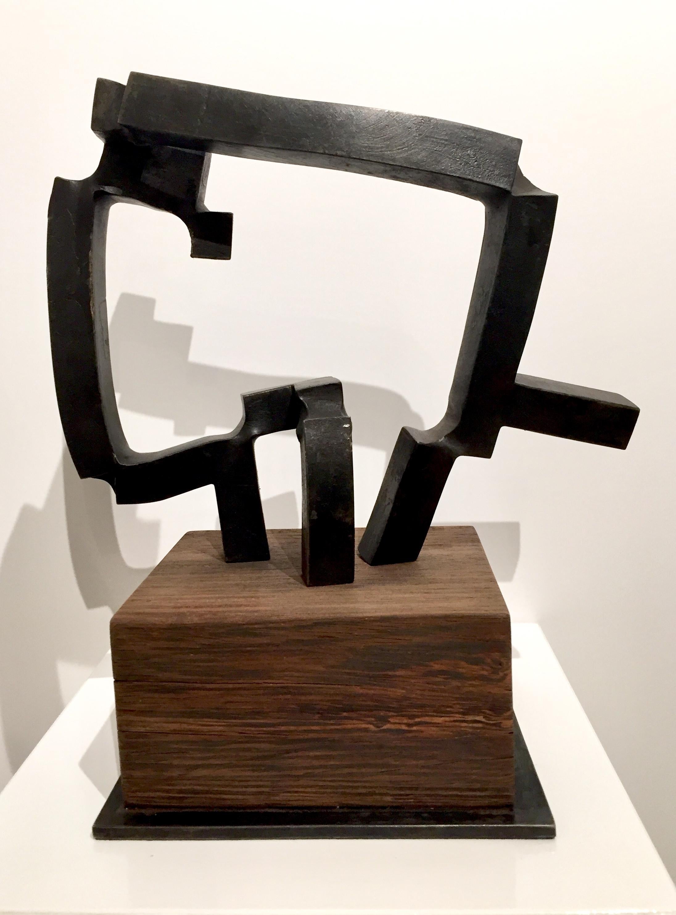 This is a 3 dimensional sculpture by Spanish abstract expressionist, Carlos Albert in dark gray forged steel on a dark brown natural wood base. 

Carlos Albert is a graduate of the School of Fine Arts at the Universidad de Complutense in Madrid,