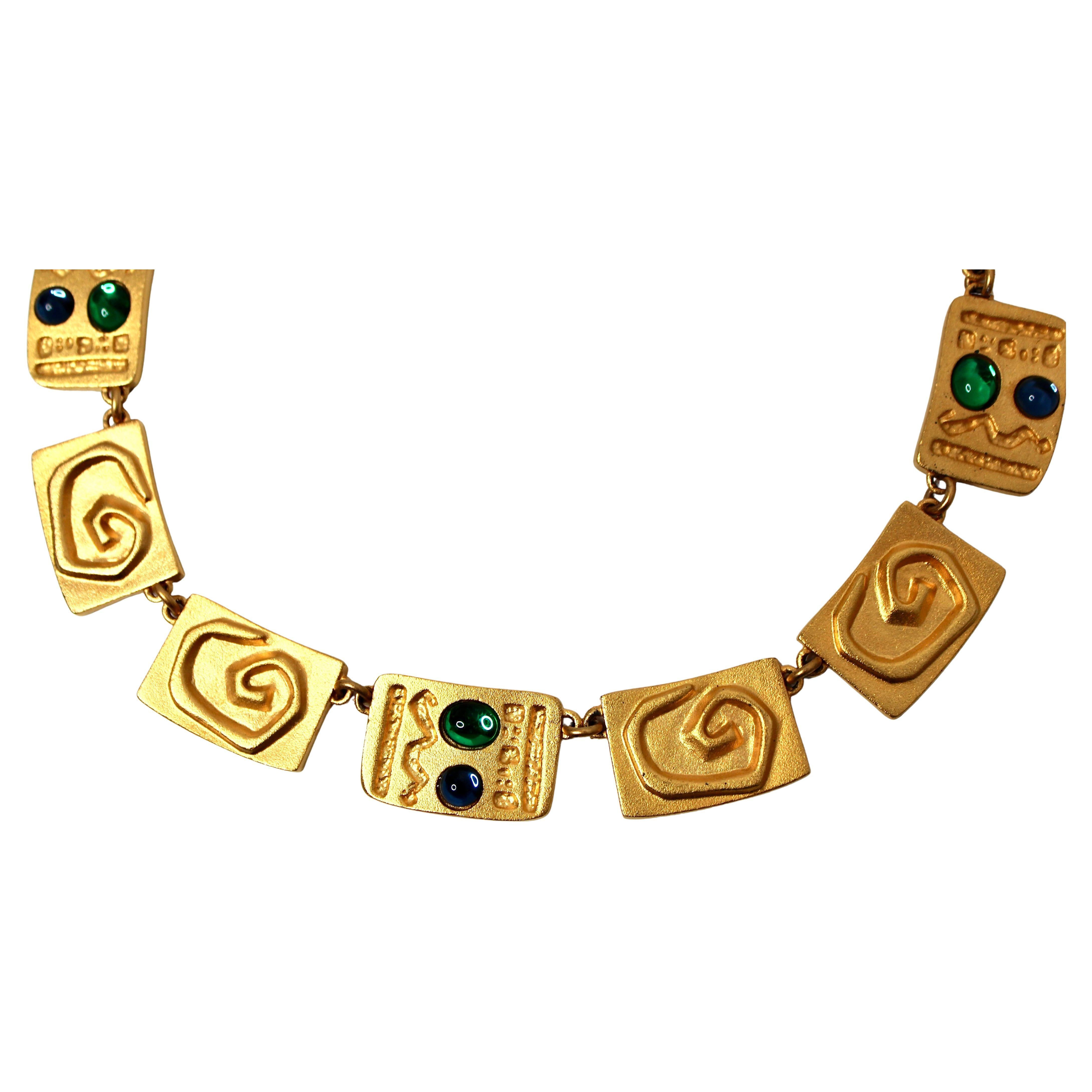 The Carlos Falchi Hieroglyph Style Carbochon Gold-Tone Necklace is a striking statement piece that seamlessly combines artistic craftsmanship with bold design. Crafted in a luxurious gold-tone finish, this necklace features a unique