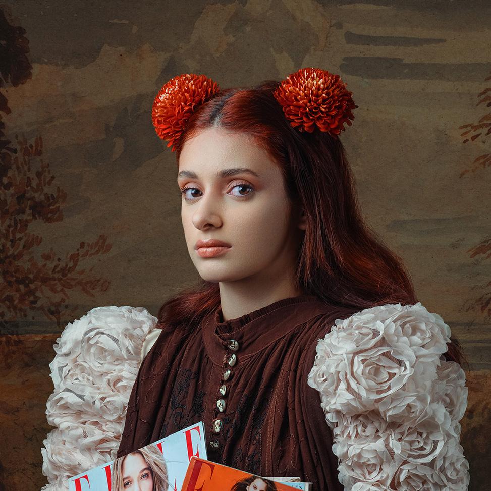 A Fashion Fairytale I displays a female figure posed in Victorian-inspired clothing while incorporating a touch of modern influences such as early 2000 magazines with bright orange Chrysanthemum's laying on the model's toned hair. The piece contains