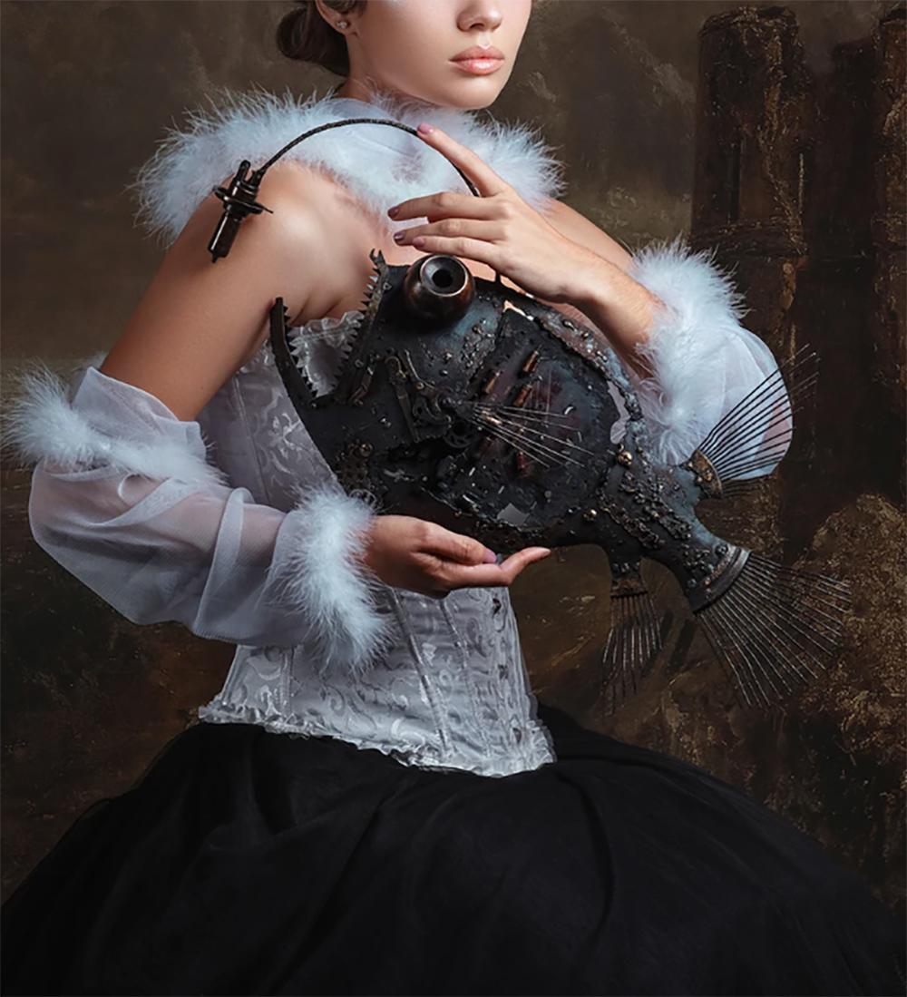 The Girl and the Fish displays a female figure posed in feathered Victorianesque clothing while incorporating a touch of 21st century influences with a steam-punk metal fish sculpture and 1960-inspired curled hair. The piece contains beautiful earth