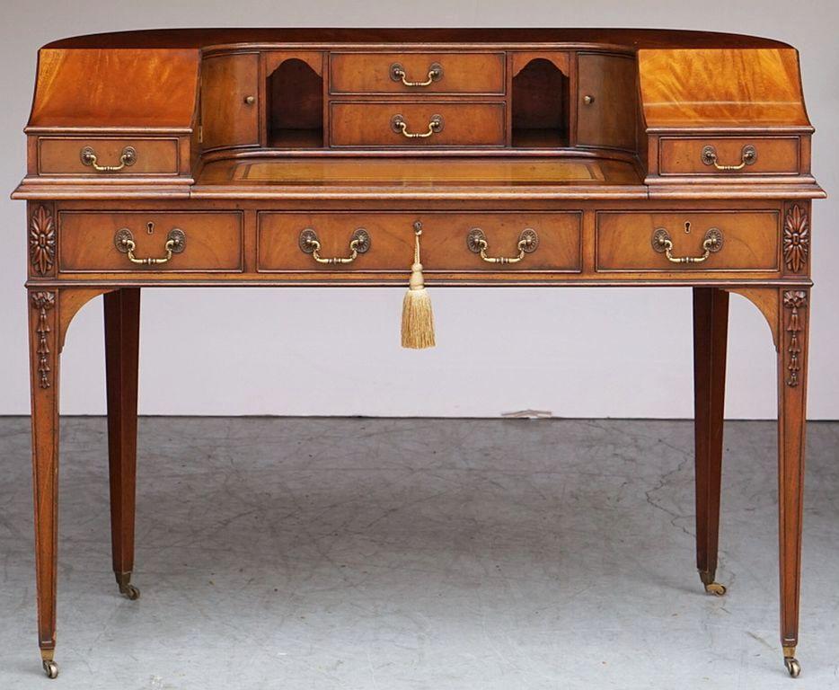 A fine English Carlton House writing table or desk of flame mahogany from the Edwardian era, with pigeon holes drawers and cupboards, and featuring a curved, pull-out slide with embossed leather top, and resting on tapering legs with rolling
