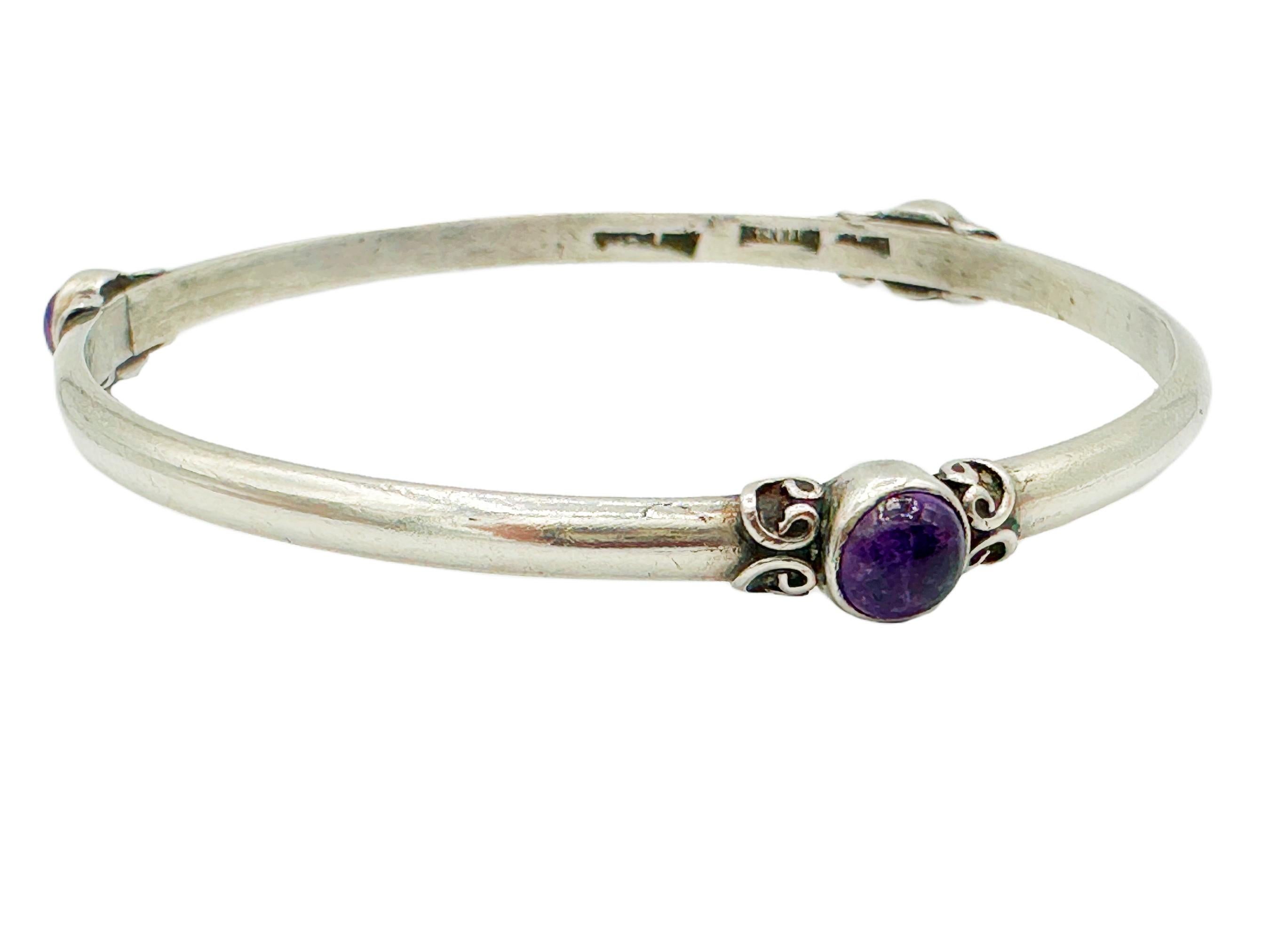 This vintage 1970s gemstone and sterling silver bangle bracelet features three bezel-set amethyst cabochons flanked with decorative silver scrollwork. It's a classic, versatile piece that's perfect for everyday wear. Each amethyst is approximately