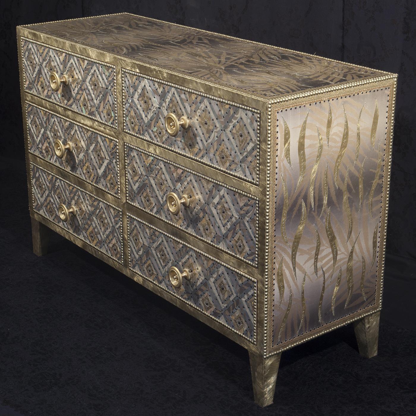 This elegant chest with three rows each featuring two drawers is made in brass and fiberglass with a striking geometrical decoration evoking an African pattern. The texture of its surface is richly adorned with metal studs for a luminous effect.