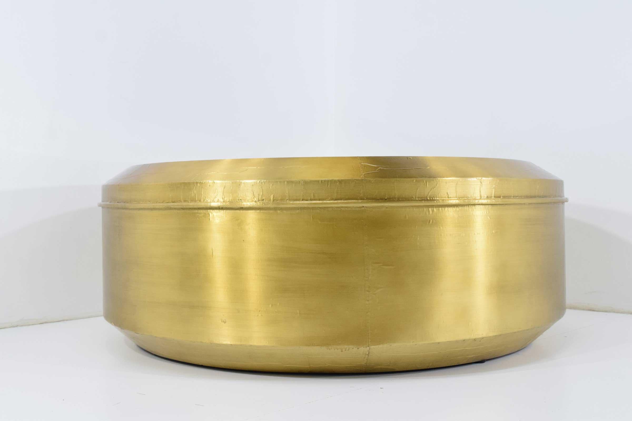 The Carnaby round cocktail table by Bernhardt has a metal base in a patinated gold leaf brass finish and an inset tempered smoked glass top over a black painted panel.